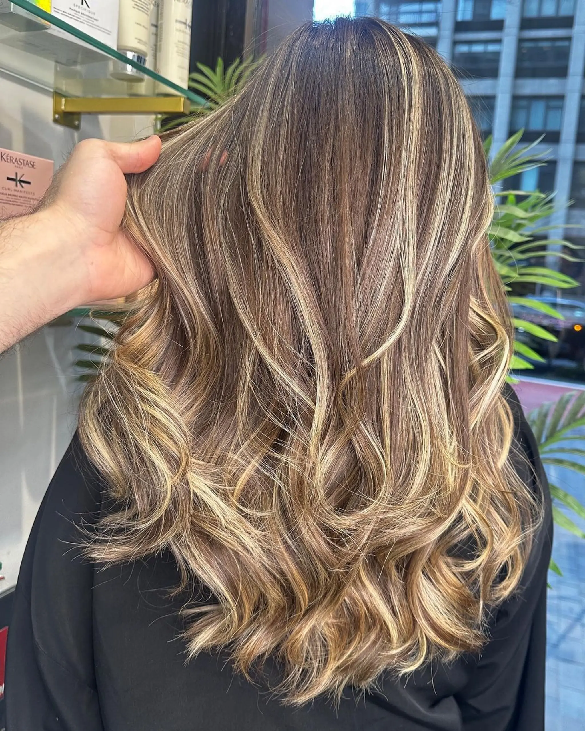 Long, wavy hair with blonde, golden, and honey highlights. Features layered locks that create a voluminous, beachy wave effect.
