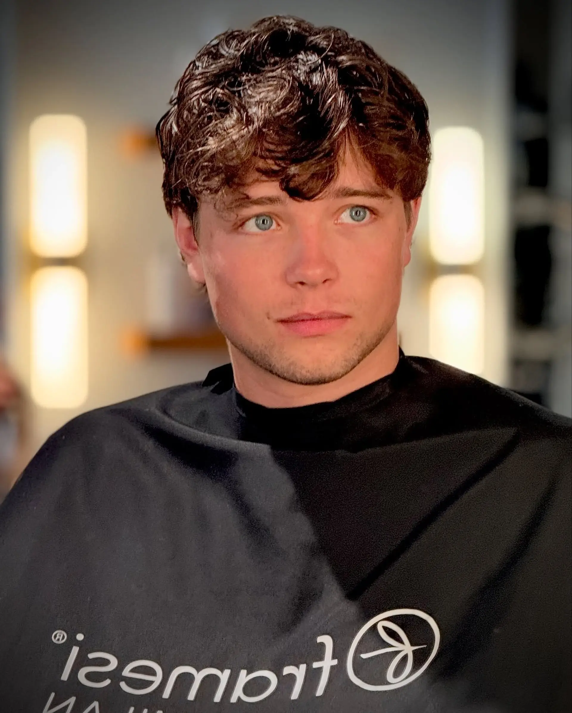 A short, textured men's crop featuring soft wavy layers styled forward into a piecey fringe with clean, tapered sides. 1