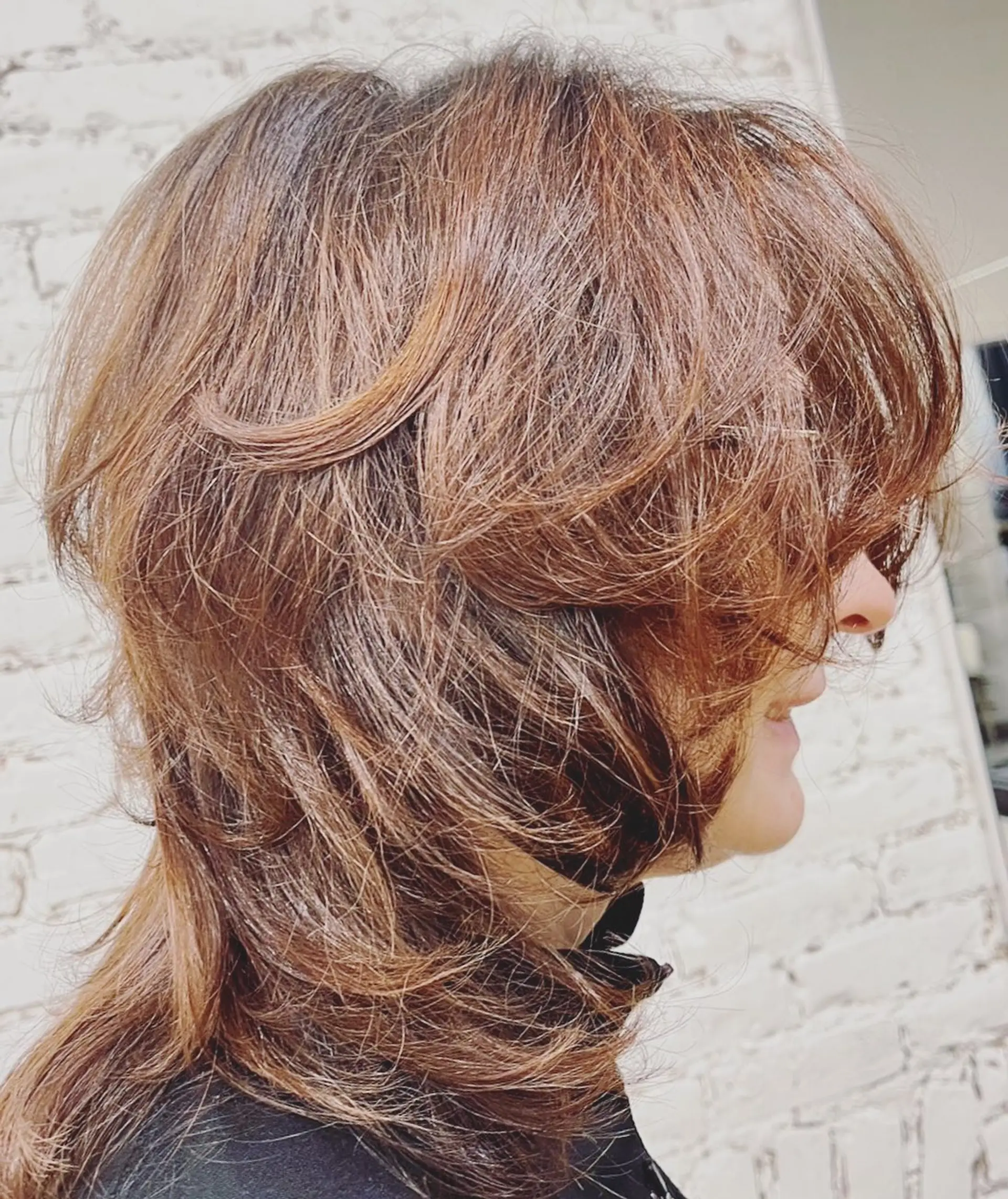 A textured soft mullet with wispy, face-framing feathered layers and long curtain bangs in a warm auburn tone. 1