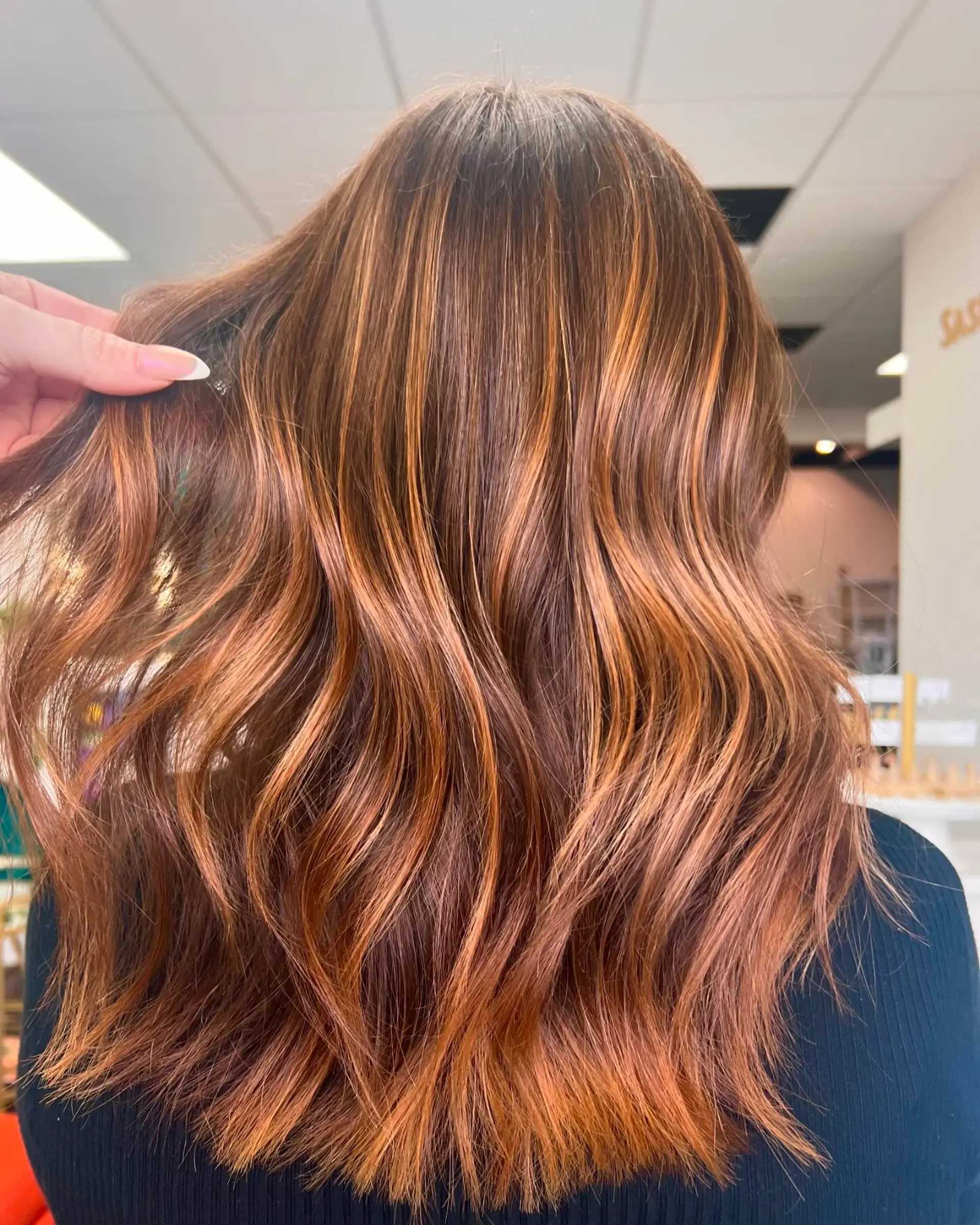 Long hair styled in soft textured waves showcasing dimensional copper and auburn highlights over a warm brown base. 1