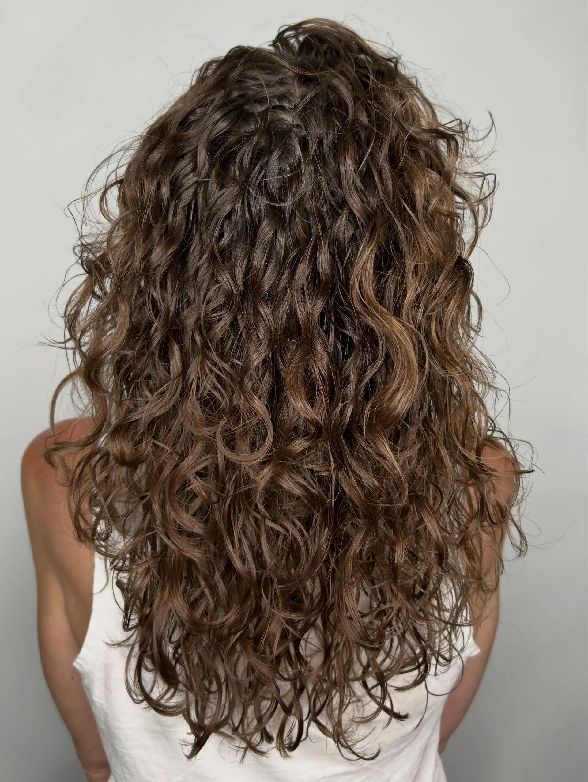 Long brunette hair styled in full, defined curls and waves created with a perm treatment. 1