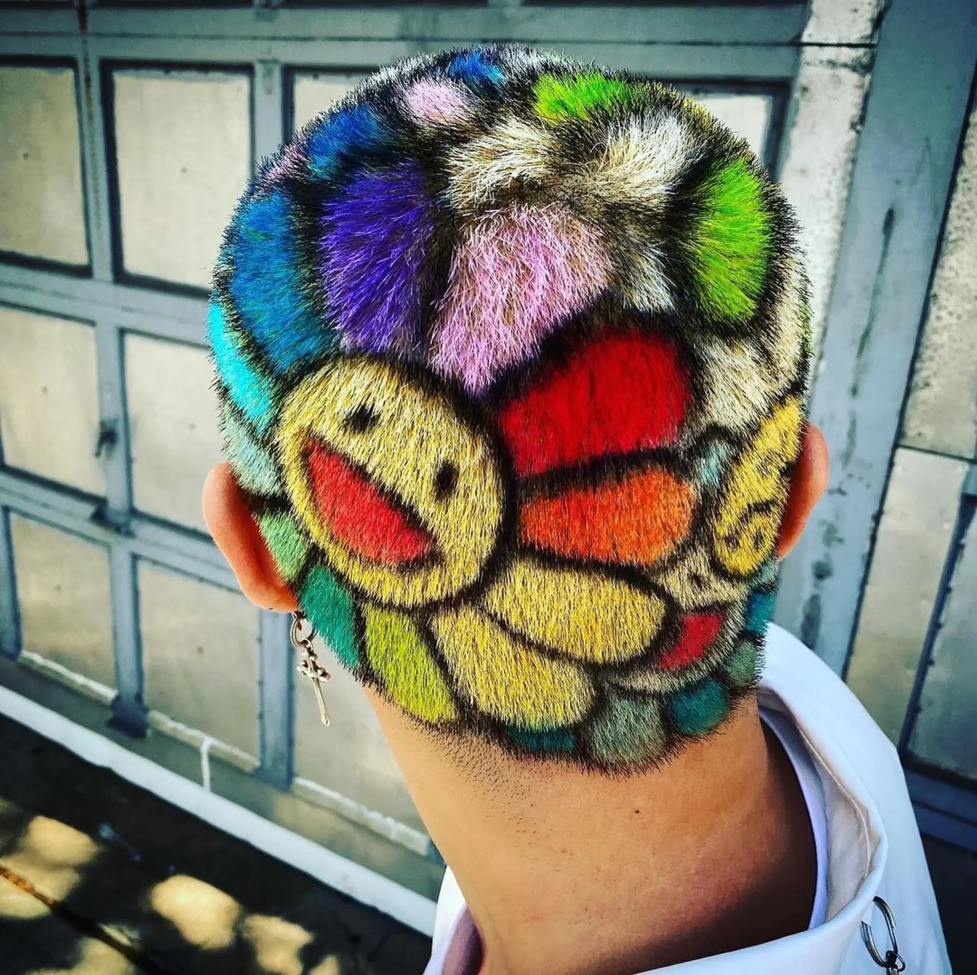 A very short buzzcut featuring a colorful mosaic design with joyful faces and petals in shades of yellow, red, purple, green, blue, orange, and black. 1