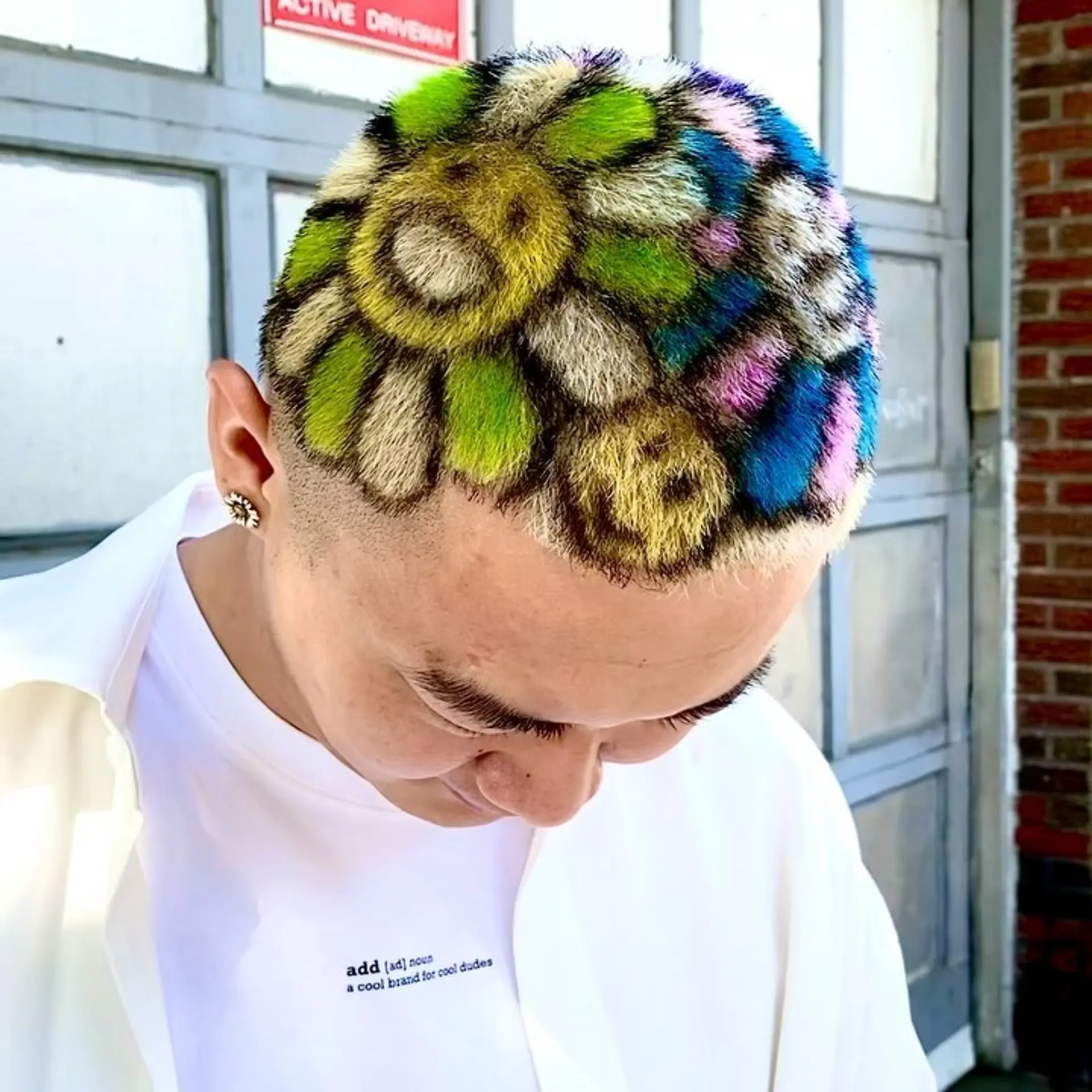 A very short buzzcut featuring a colorful mosaic design with joyful faces and petals in shades of yellow, red, purple, green, blue, orange, and black. 2