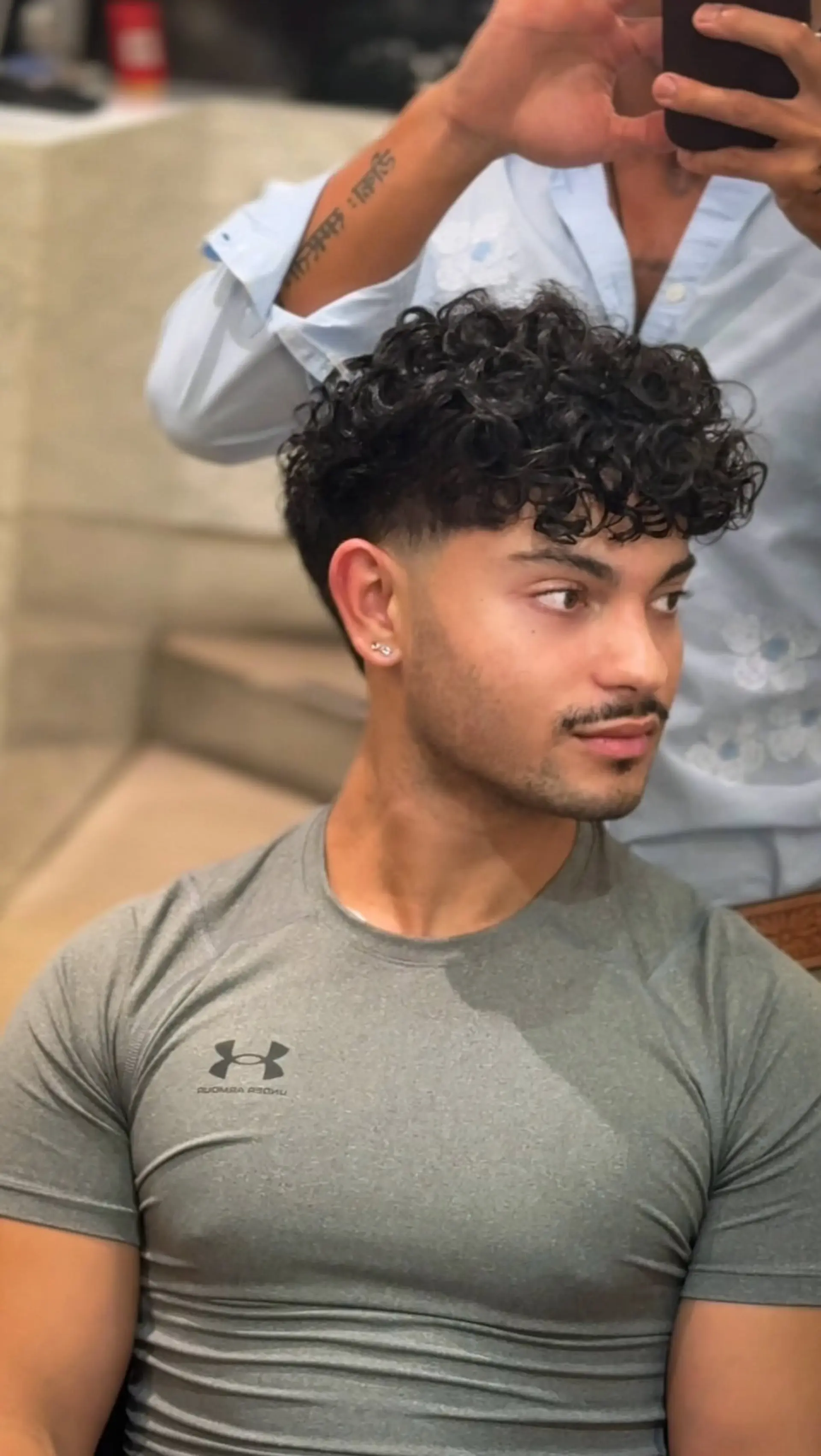 A modern men's cut showcasing defined curls on top paired with a clean low taper fade around the ears and neckline. 1