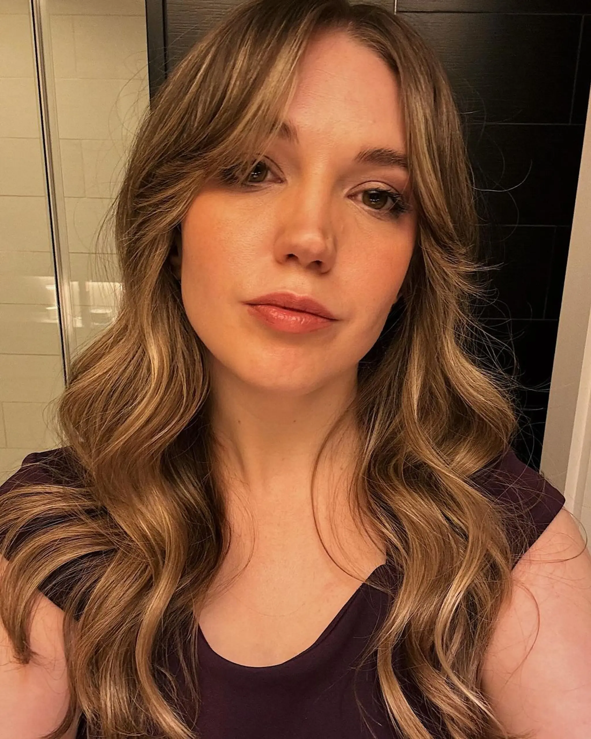 Long, wavy hair with honey blonde, light brown, and golden highlights. Center part with soft waves and face-framing strands, creating a natural, sun-kissed look.