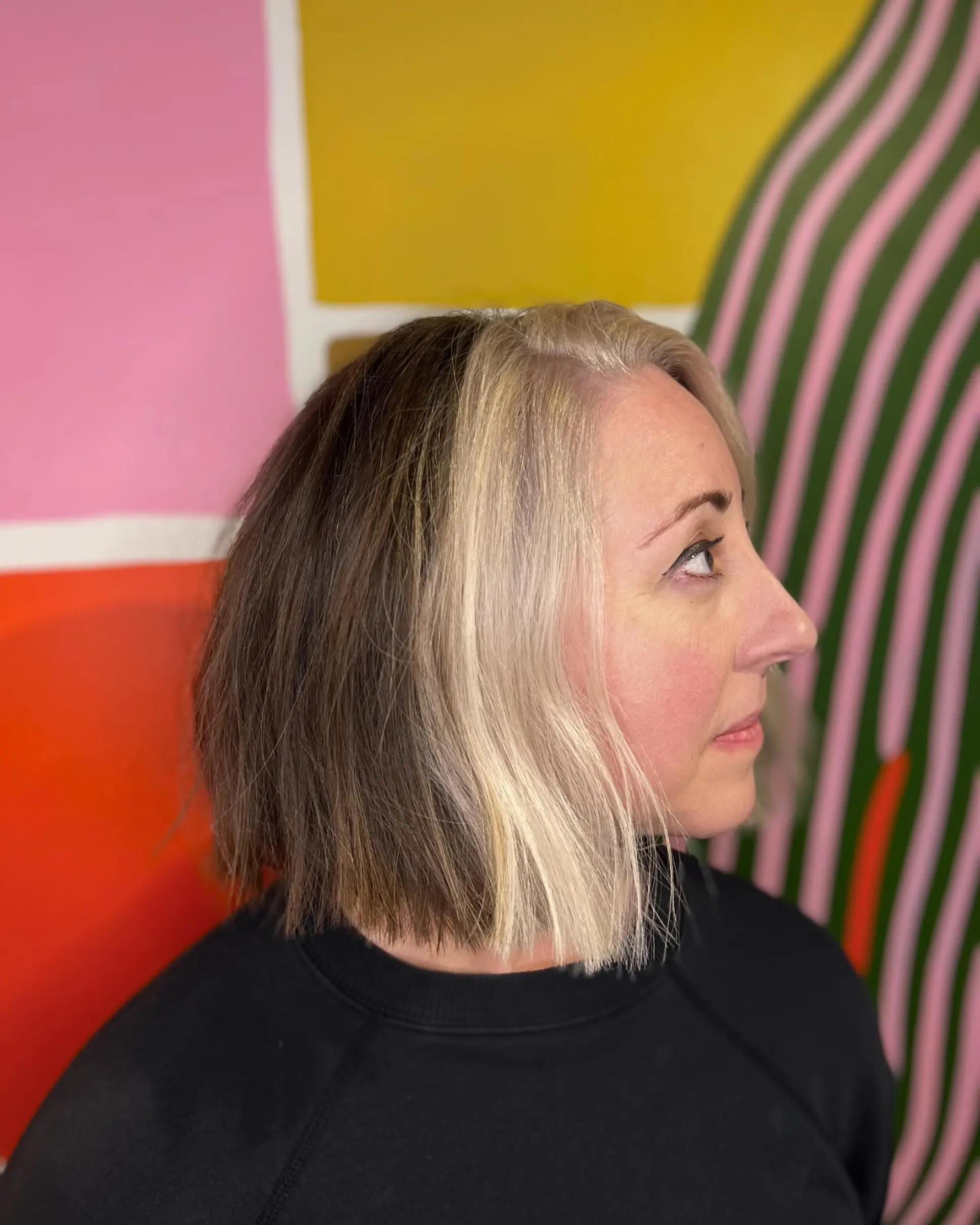 A textured blunt bob cut to the chin with a striking, high-contrast platinum blonde money piece block against deep ash brown hair. 1