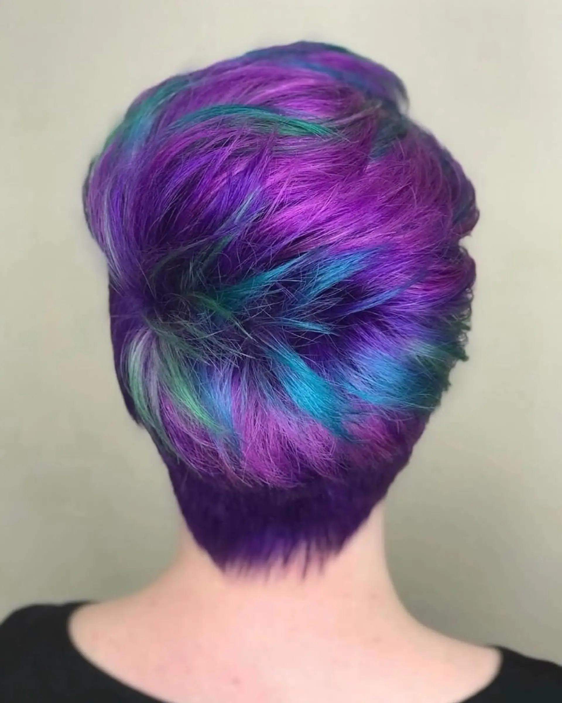 A textured short pixie haircut featuring vivid shades of purple, teal, and bright blue throughout the crown and tapered neckline. 1