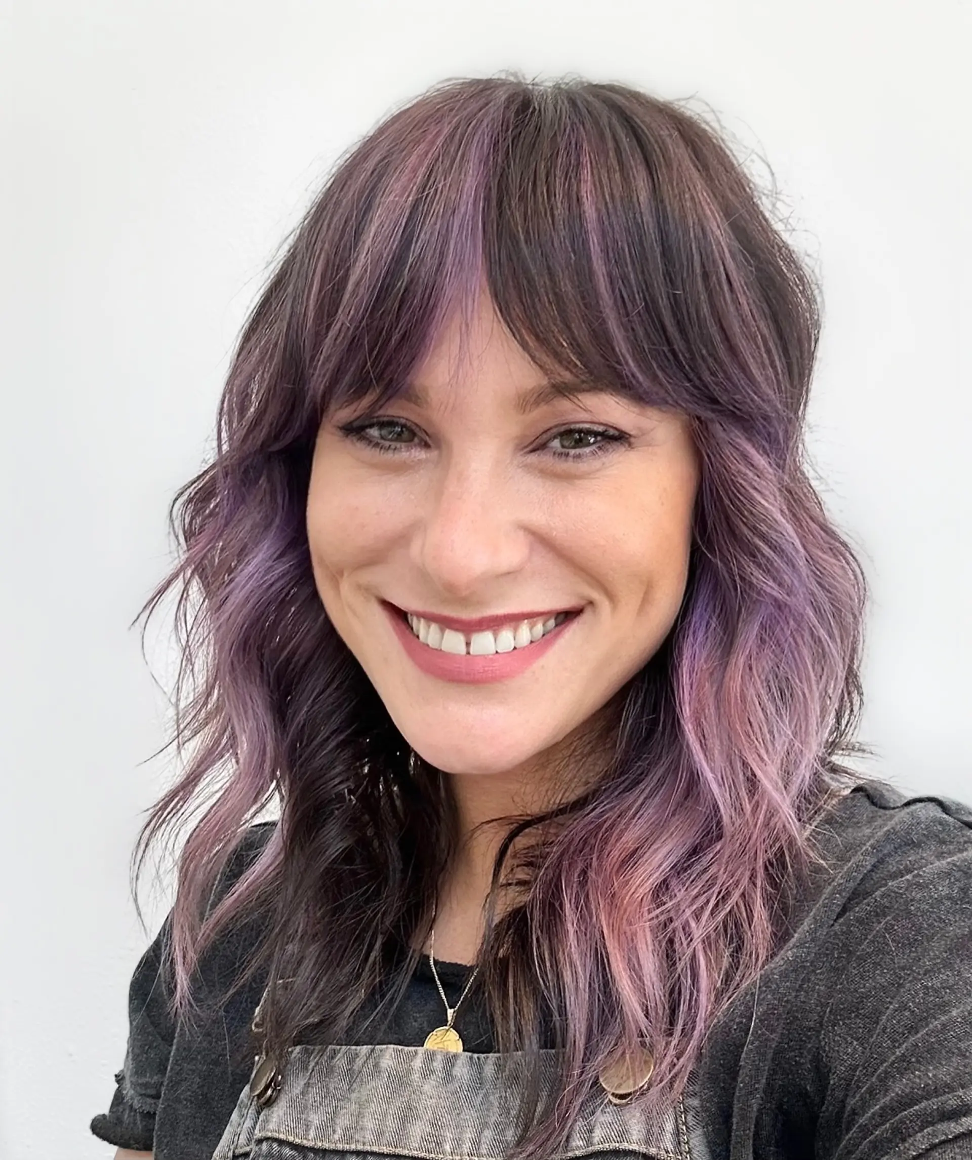 Medium-length layered shag haircut with curtain bangs and pastel purple highlights over a dark base. 1