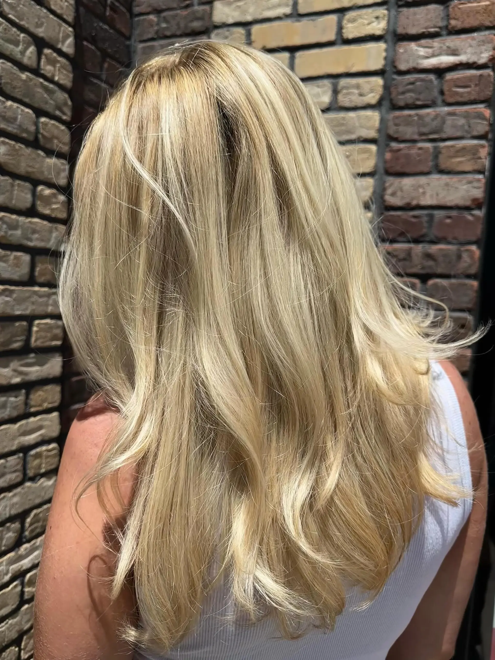 Long sun-kissed blonde hair with dimensional highlights cut in layers and styled with soft flipped waves. 1