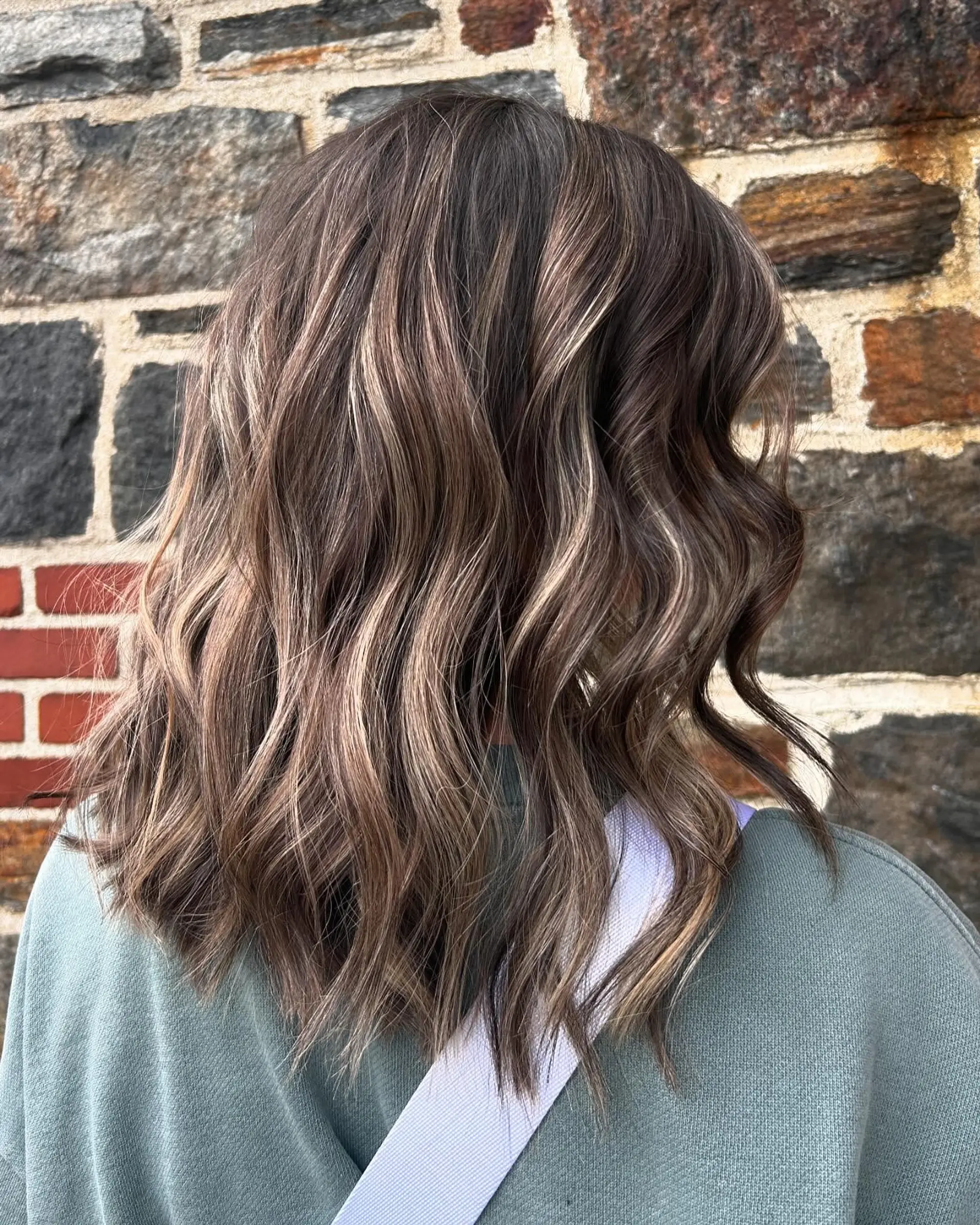 Medium-length dimensional brunette hair featuring finely blended highlights and lowlights, styled in loose textured waves. 1
