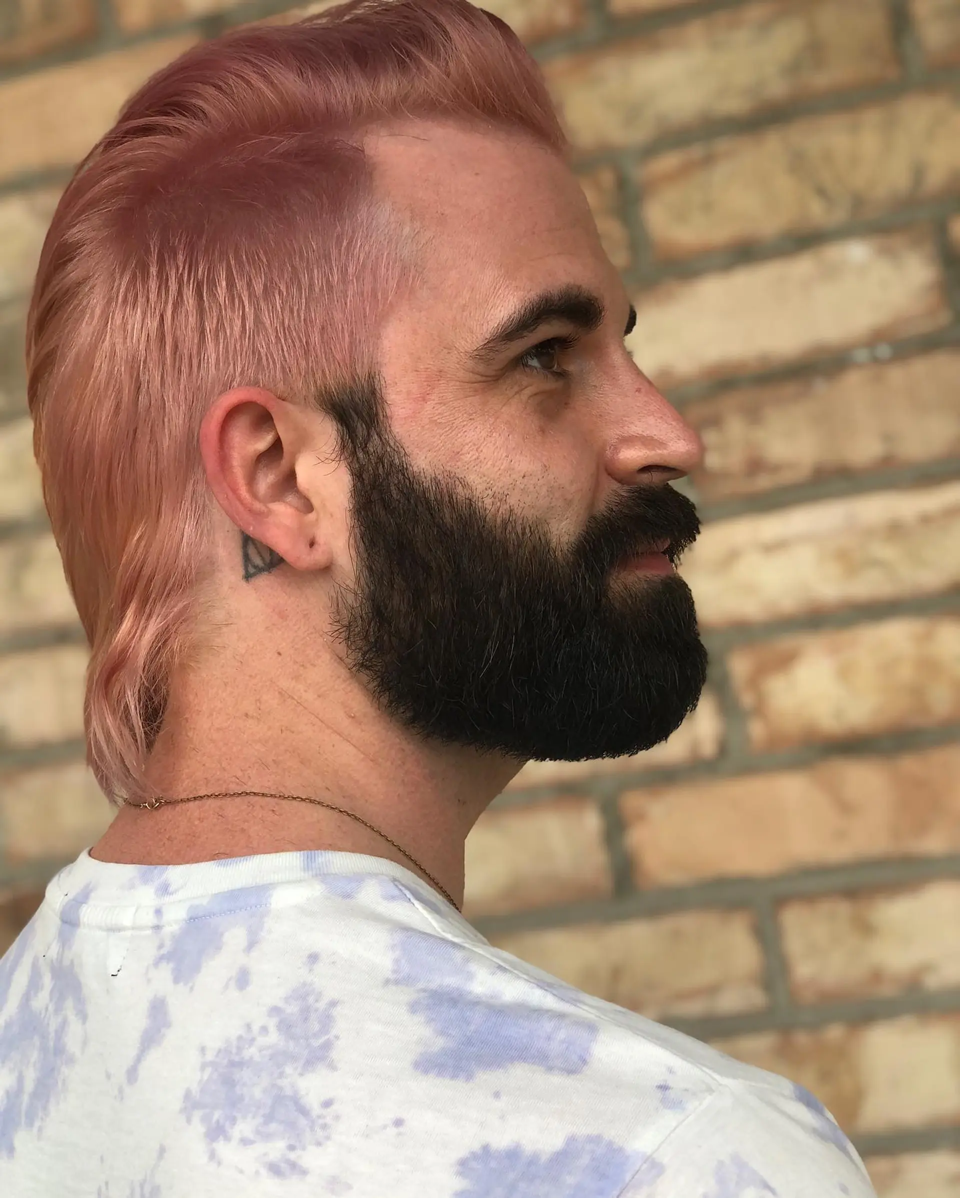 A soft pastel pink modern mullet with shorter faded sides and longer textured length on top extending down the nape. 1