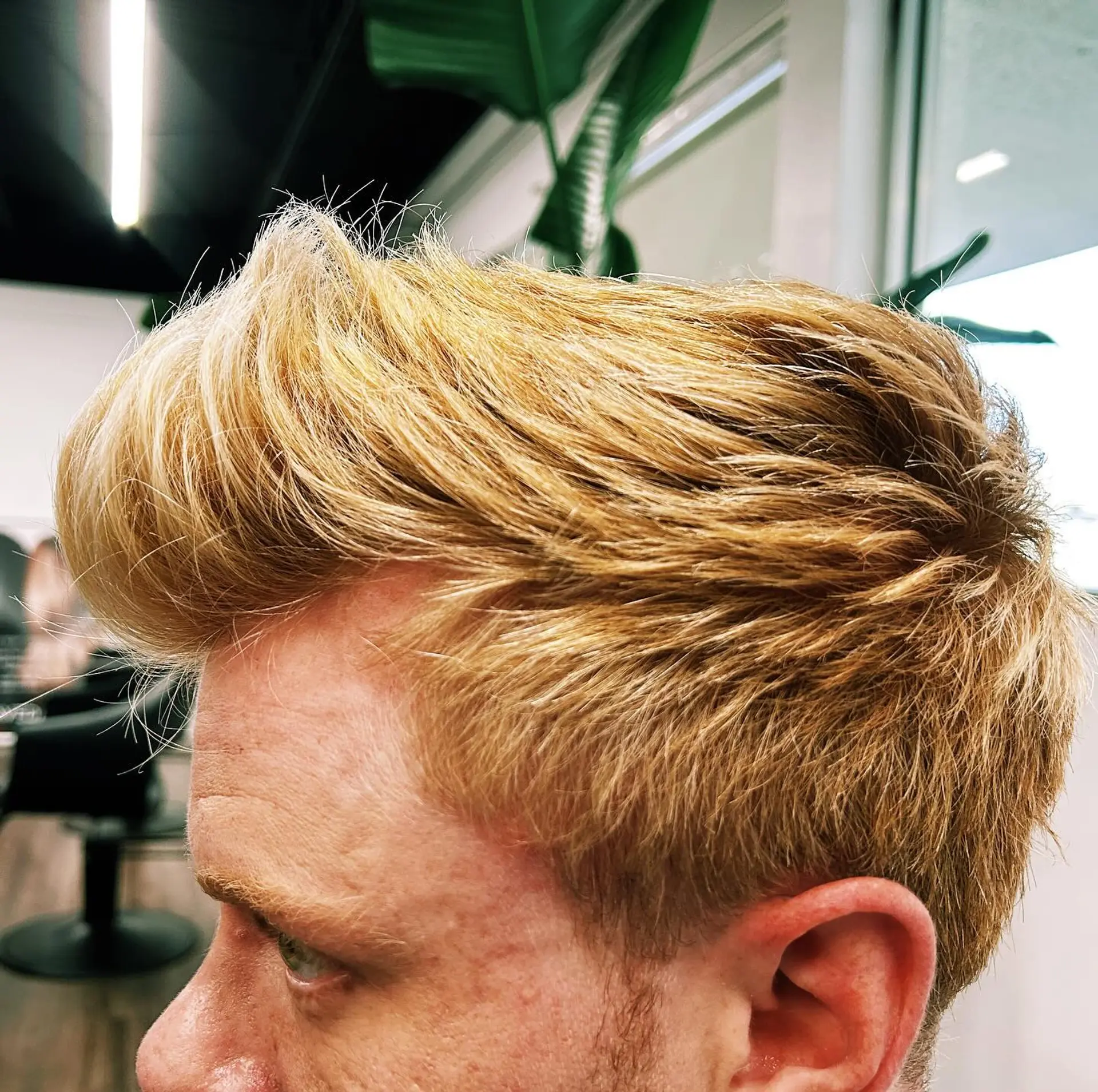 A men's short haircut styled into a textured quiff with warm golden blonde highlights. 1