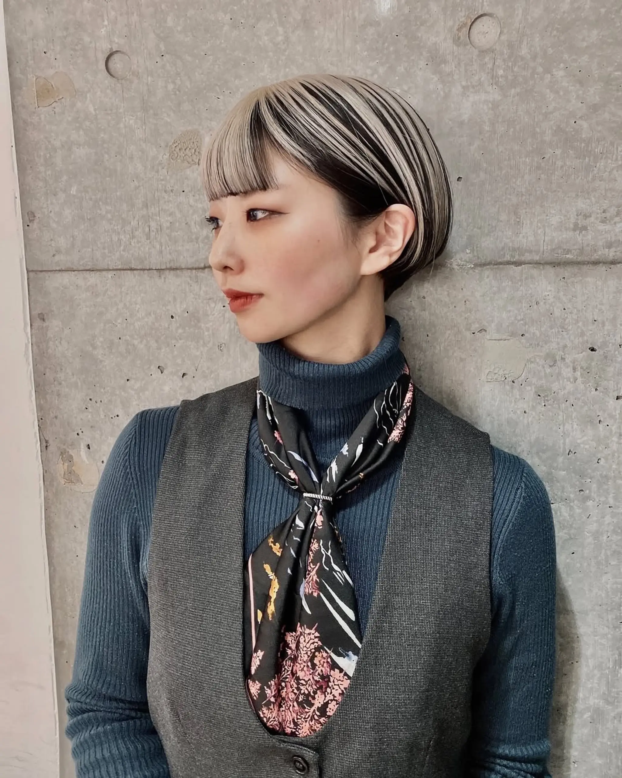 A short, sleek, layered bob with platinum blonde and ash brown shades, featuring a heavy fringe and side-swept bangs for a modern look.