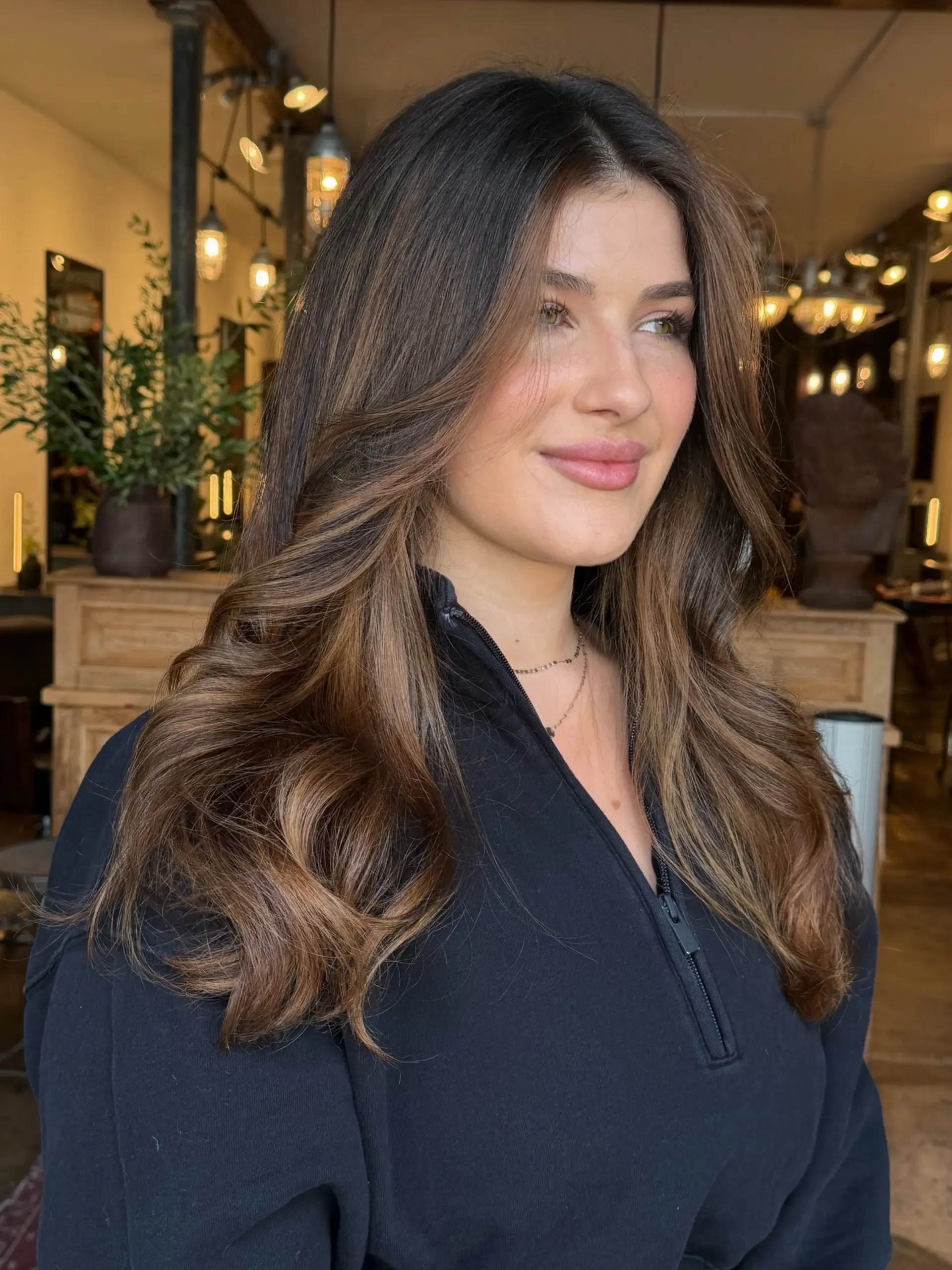 Long, soft wavy brunette hair featuring seamless hand-painted warm caramel balayage highlights and face-framing layers. 1