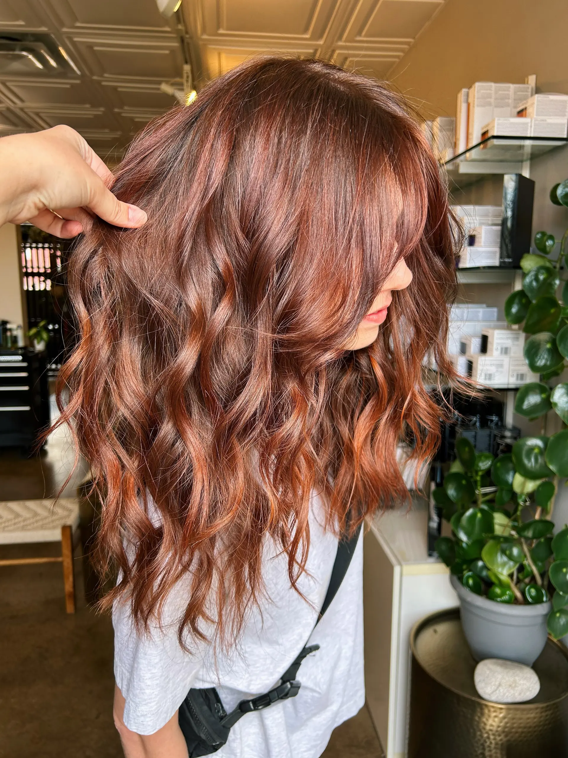 Long, tousled wavy hair colored in a rich dimensional copper with face-framing curtain bangs. 1