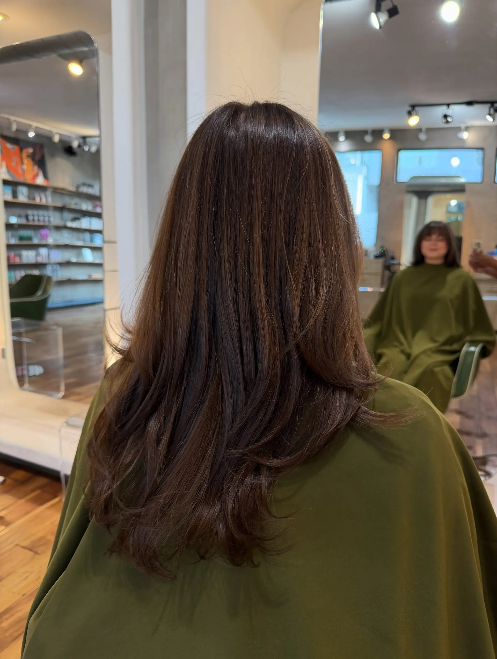 Long brunette layered haircut featuring seamless, blended layers with soft flip-under ends and front fringe visible in the mirror reflection. 1