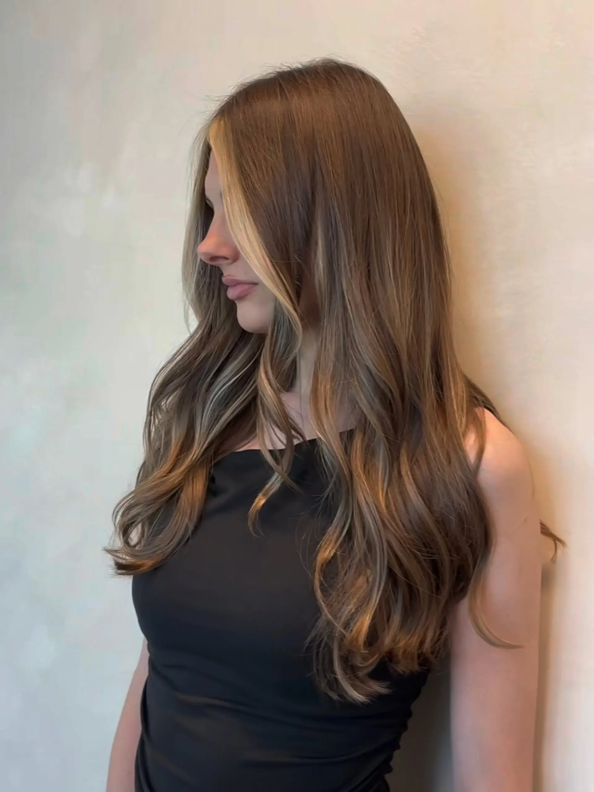 Long layered light brown hair styled in soft loose waves with blonde face-framing highlights. 1