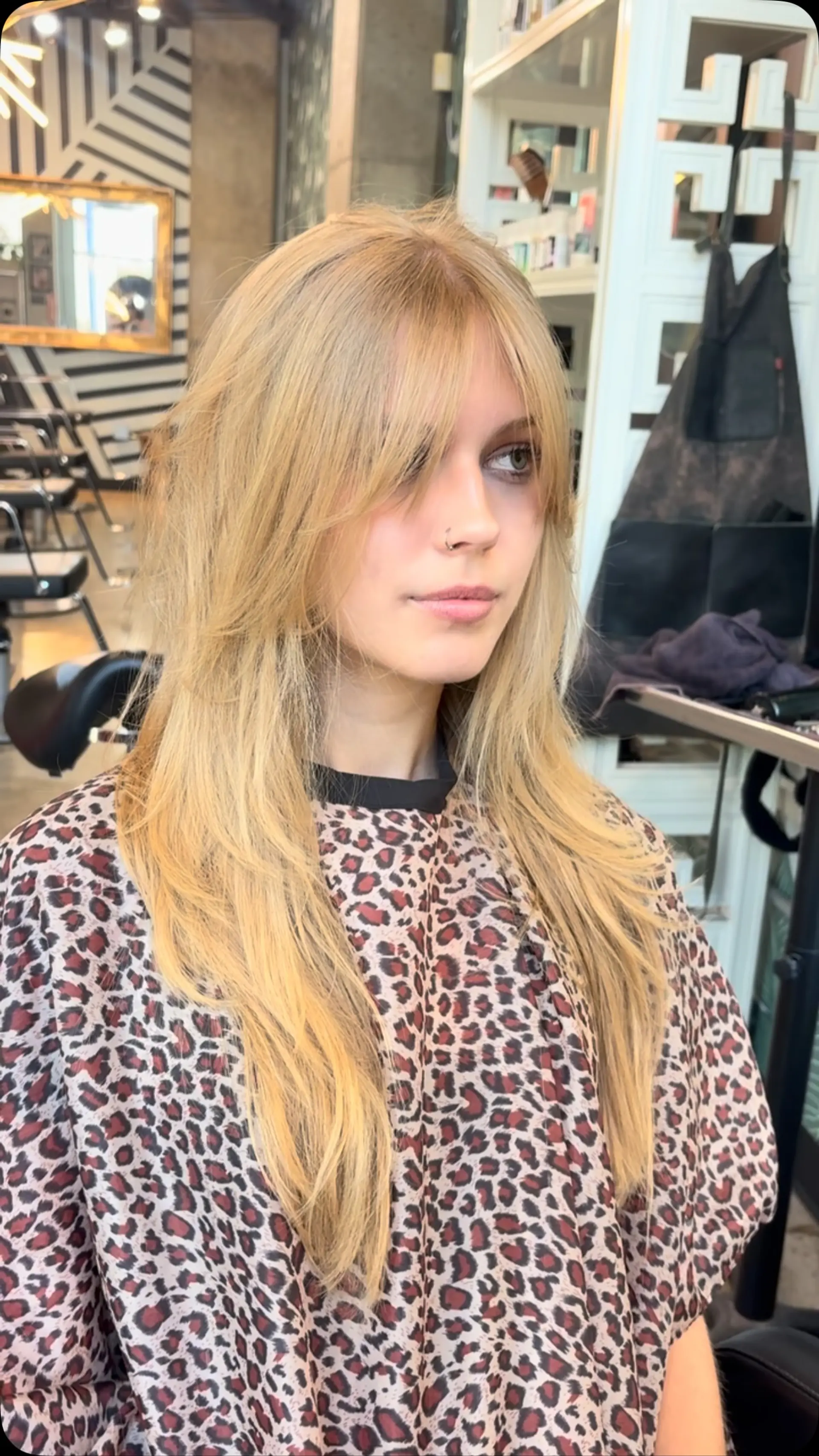 Long warm blonde hair cut with soft, face-framing layers and wispy curtain bangs. 1