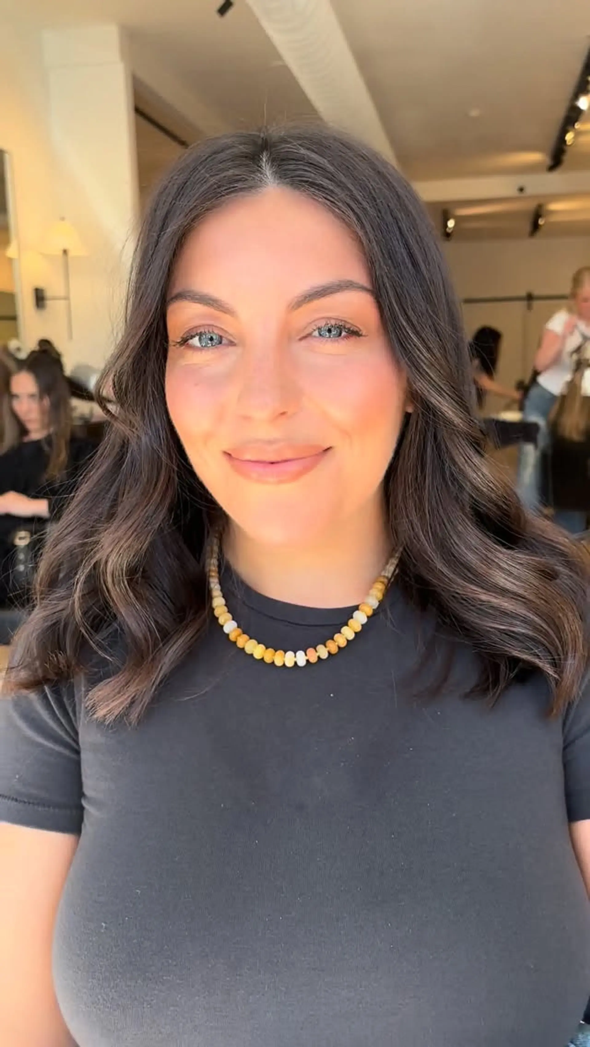 Medium-length dark brunette hair parted in the middle and styled with soft, loose waves. 1