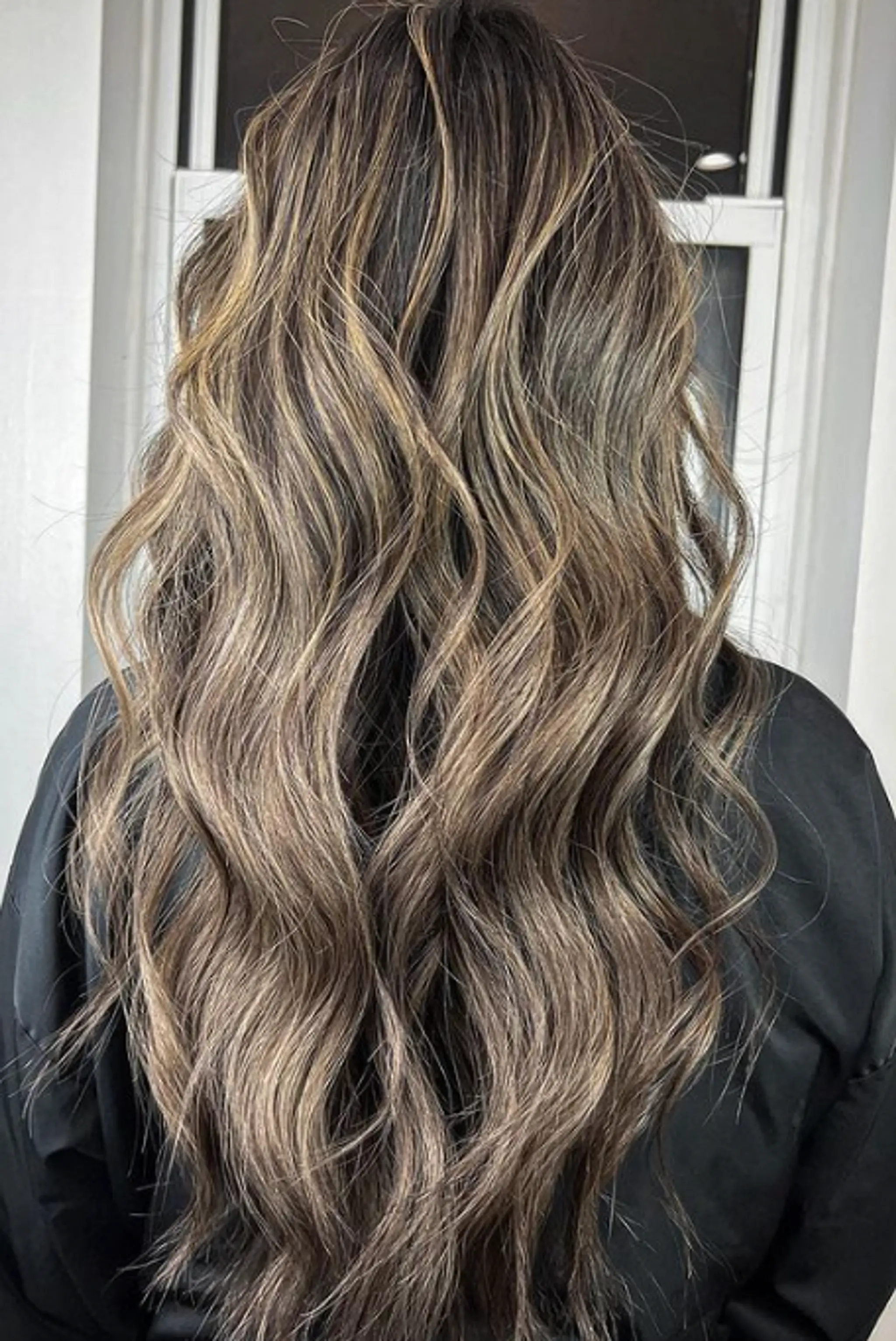 Very long, wavy hair with golden blonde and light brown balayage, loose beach waves, and a glossy finish with a layered look.