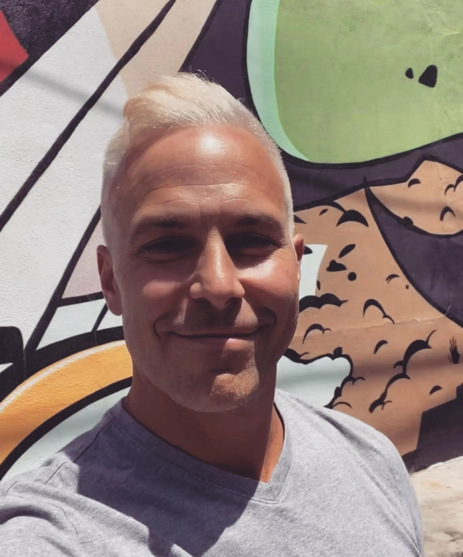 A clean, short haircut with tapered sides and a textured, swept-up platinum blonde top. 1