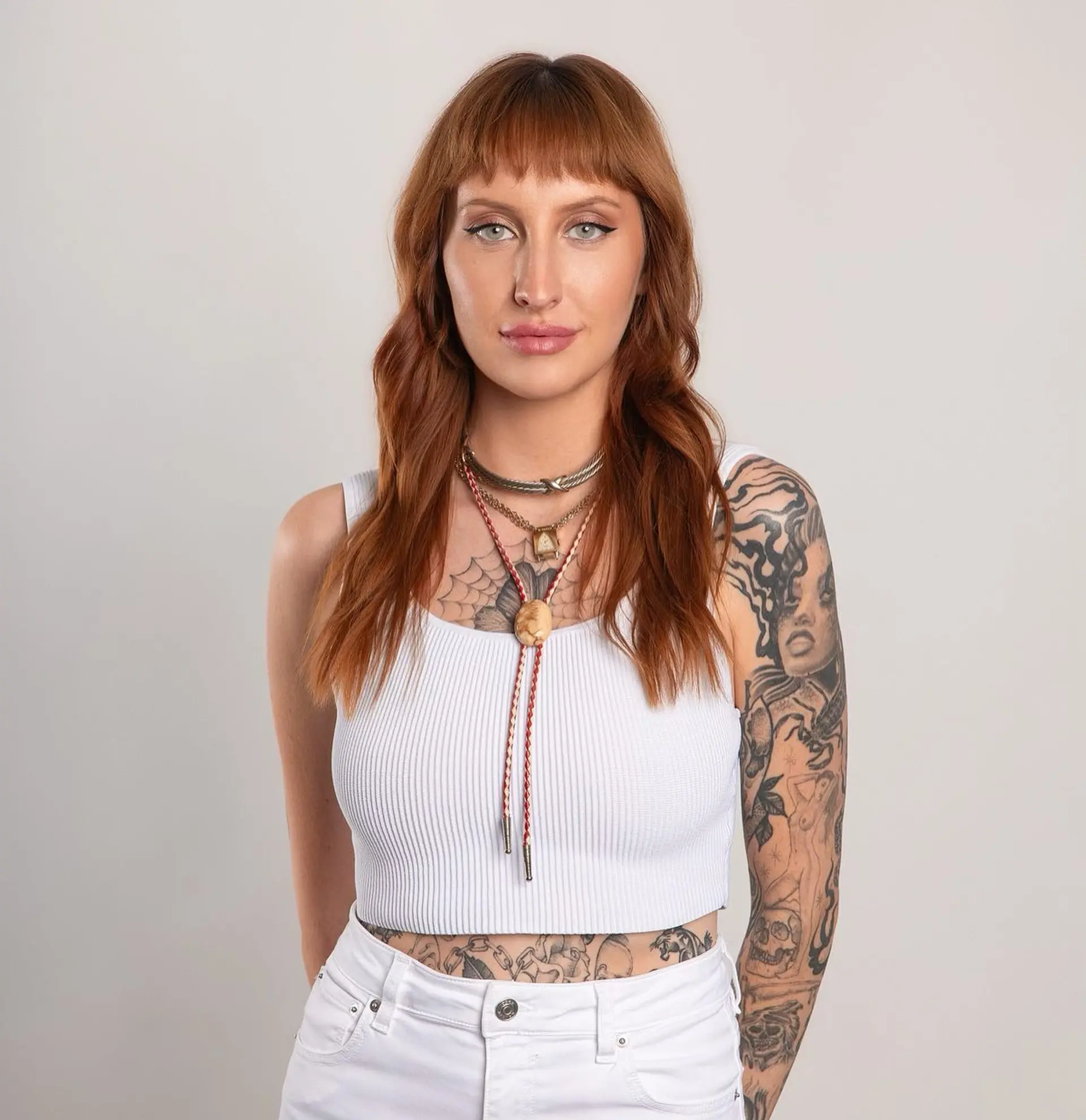 Medium-length copper hair styled in loose waves with straight fringe bangs. 1
