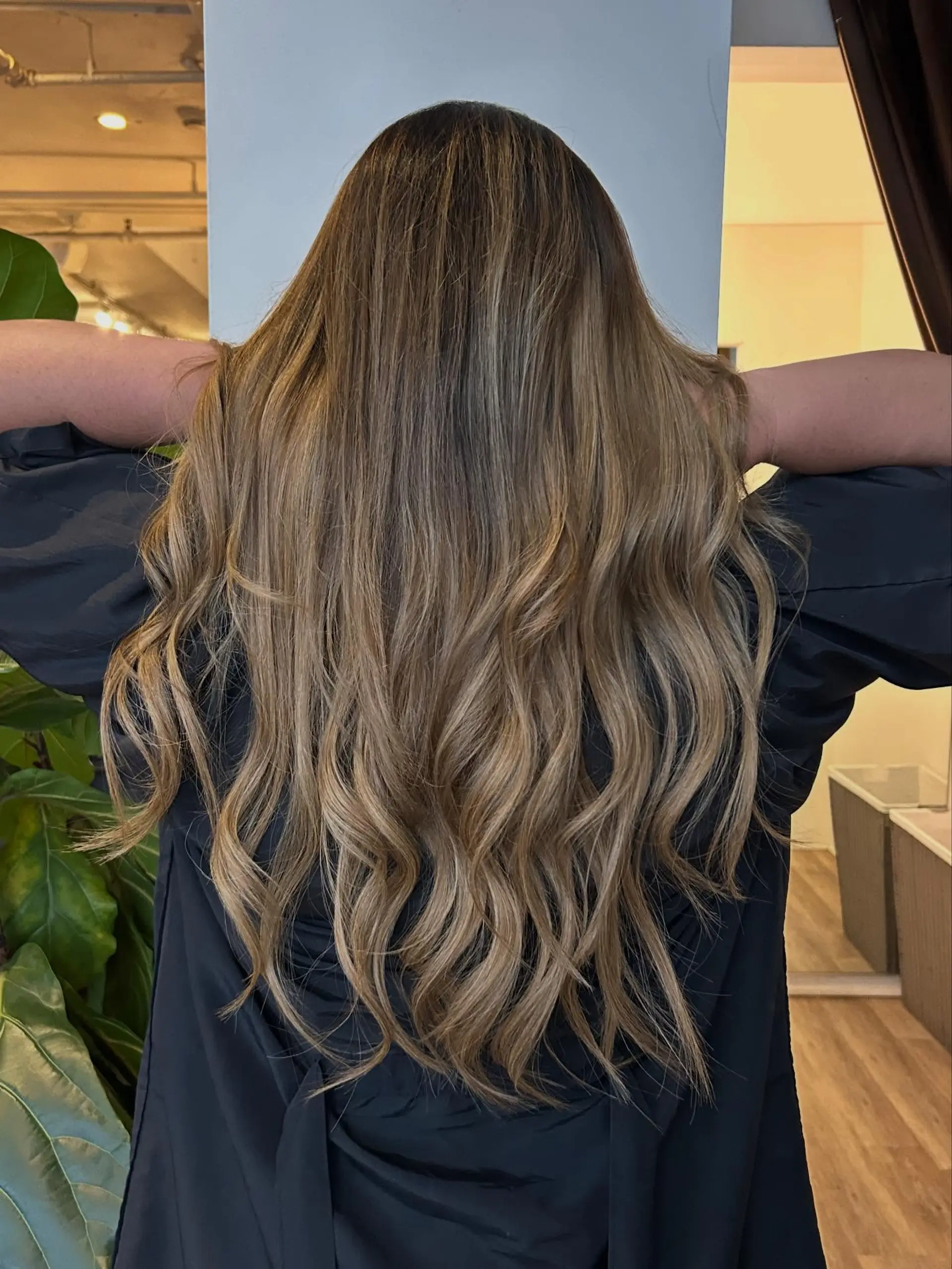 Long, layered bronde hair featuring seamless dimensional balayage highlights styled with gentle loose waves. 1