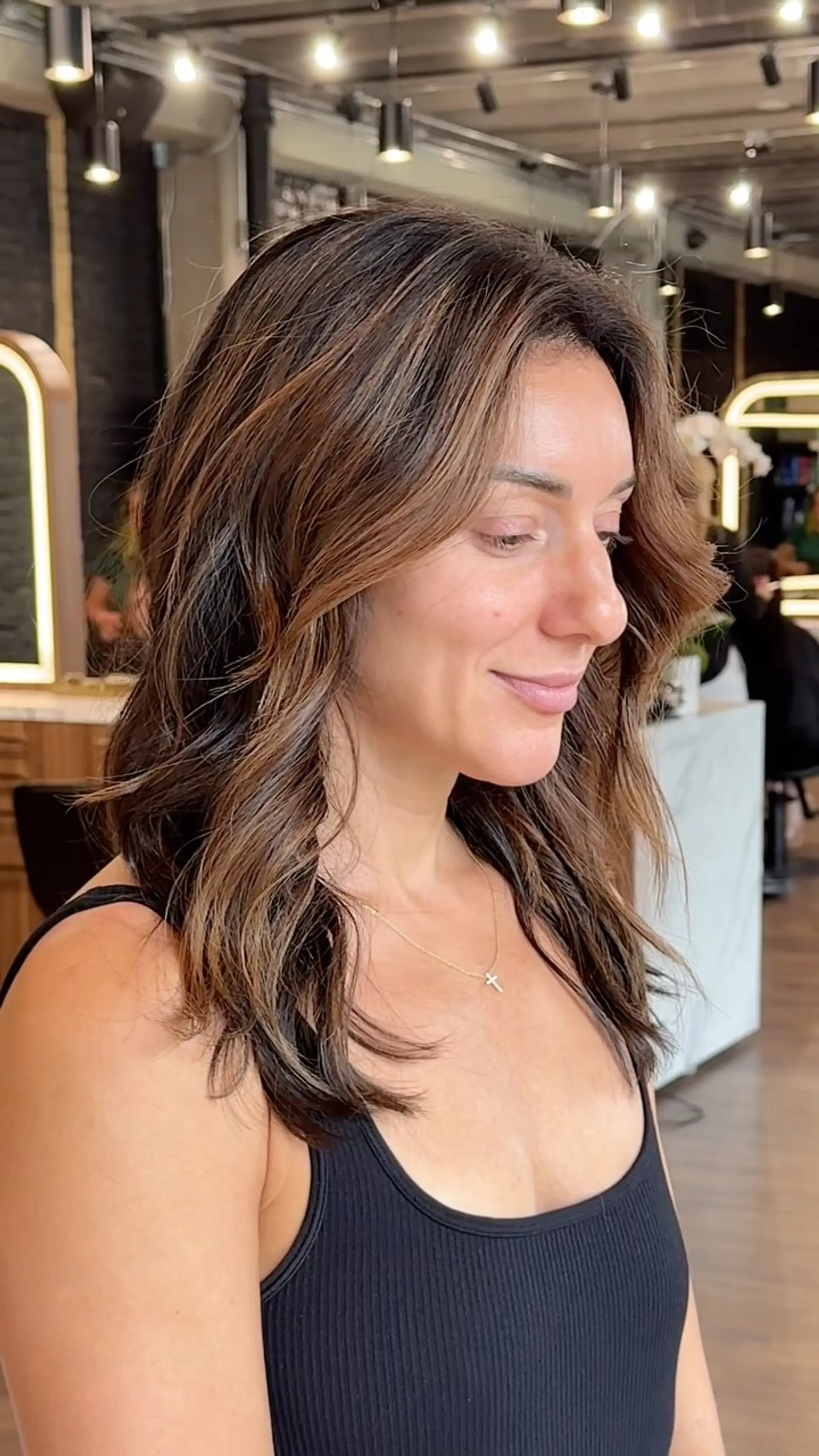 Medium-length brunette hair styled with soft caramel highlights and loose, face-framing textured waves. 1