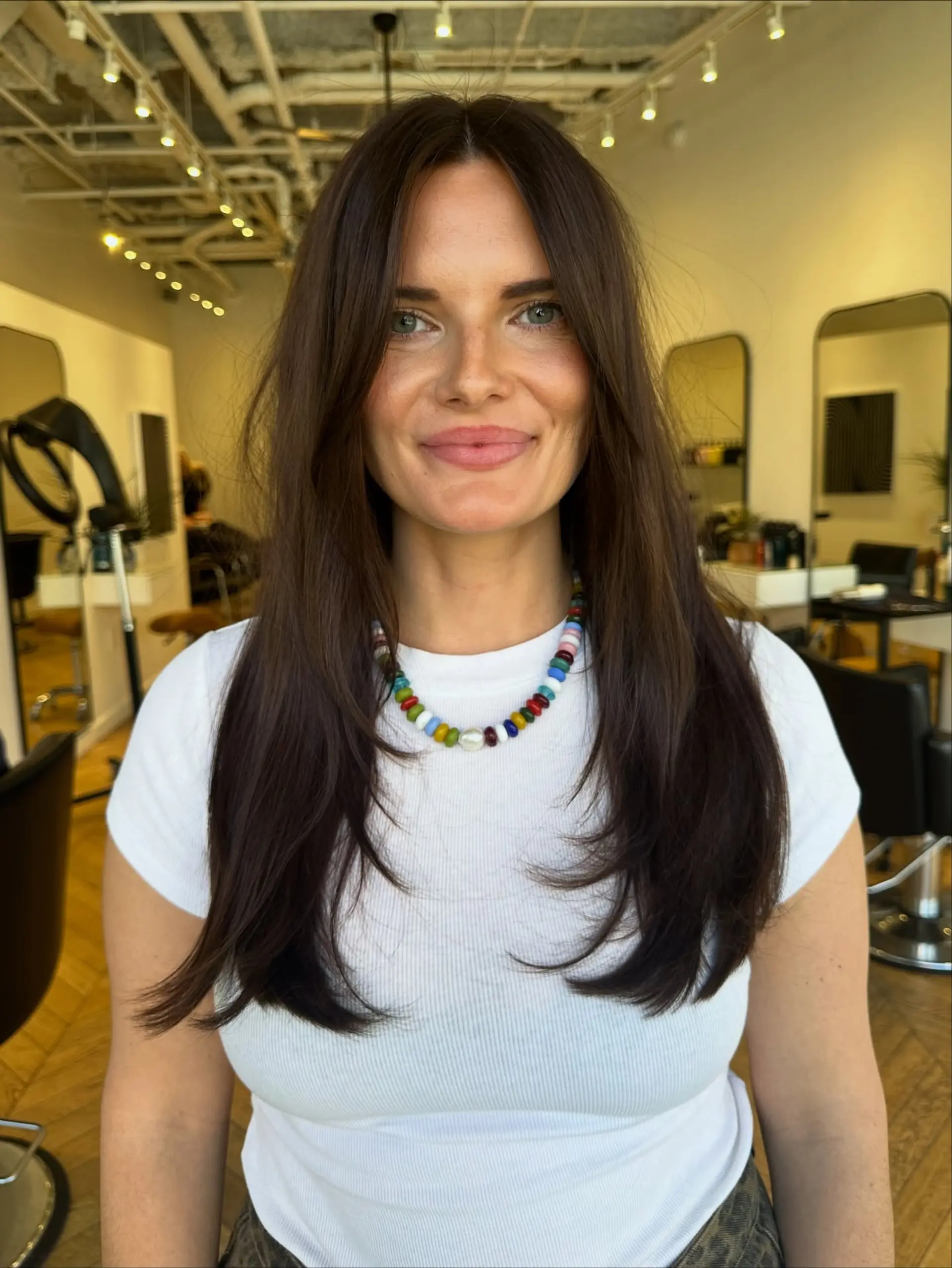 Long rich dark brown hair featuring long layers and soft face-framing curtain bangs styled straight with gentle inward curve. 1