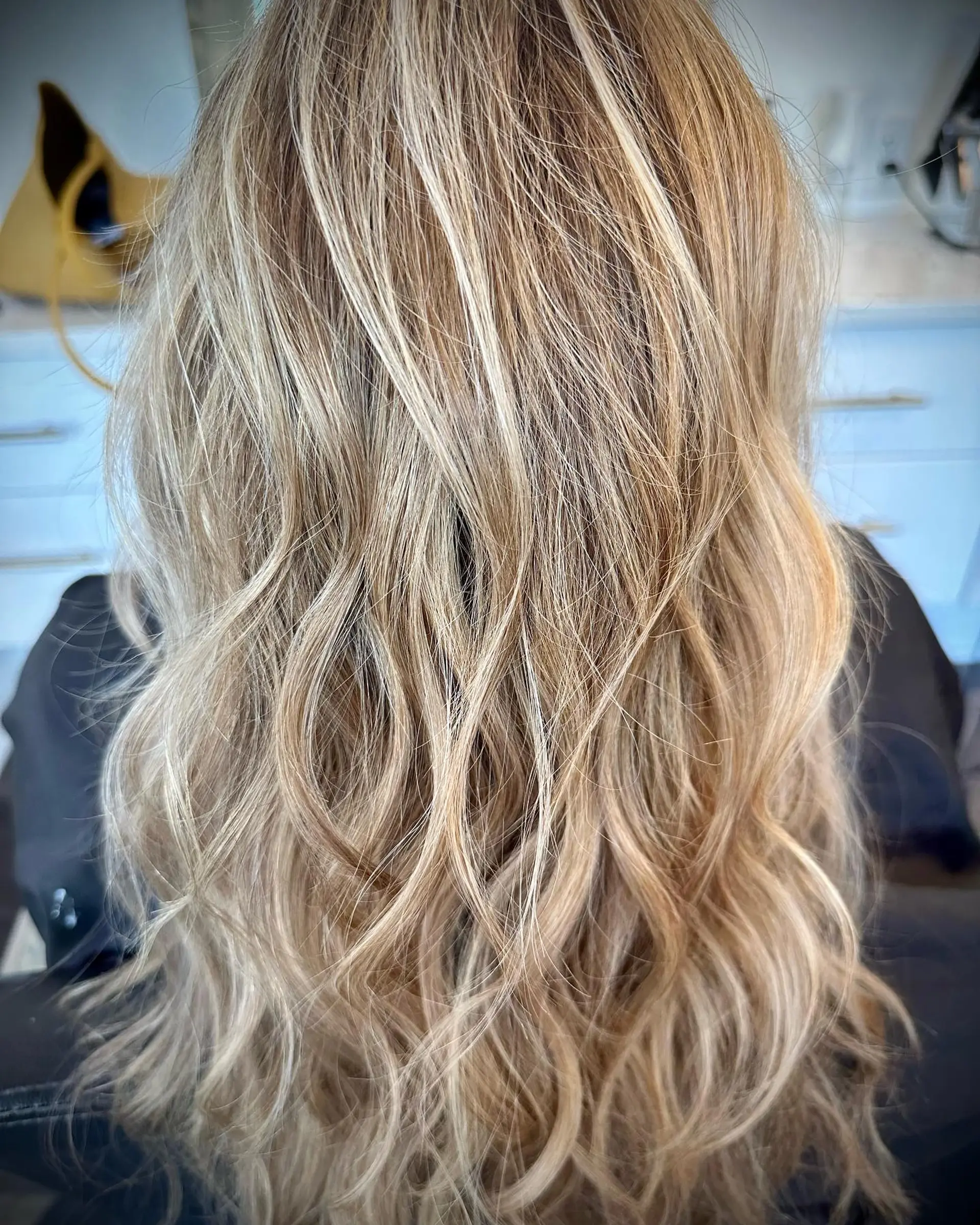 Long multi-tonal blonde balayage styled with tousled, textured beach waves. 1