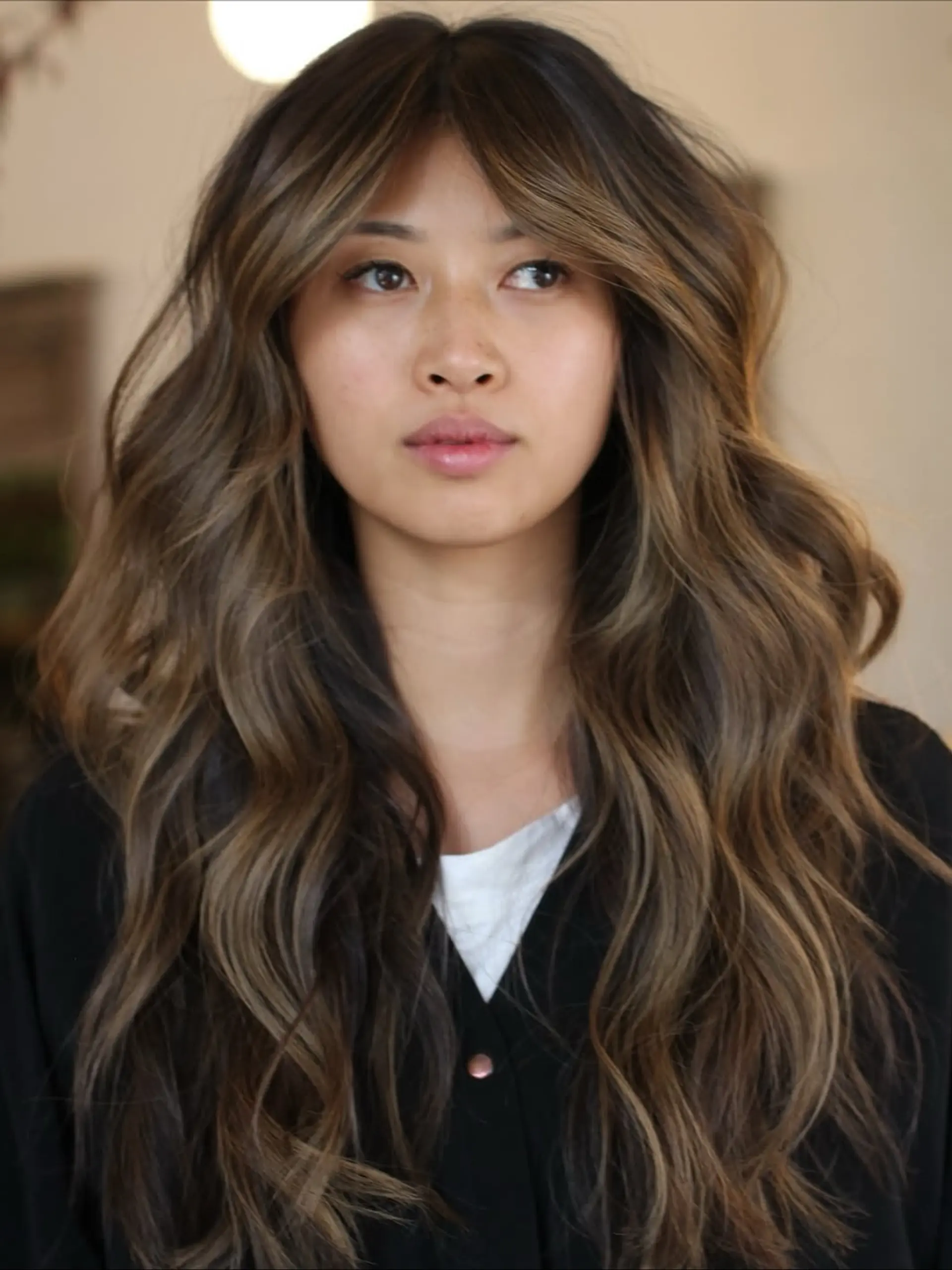 Long wavy brunette hair highlighted with warm autumnal caramel tones and styled with center-parted curtain bangs. 1