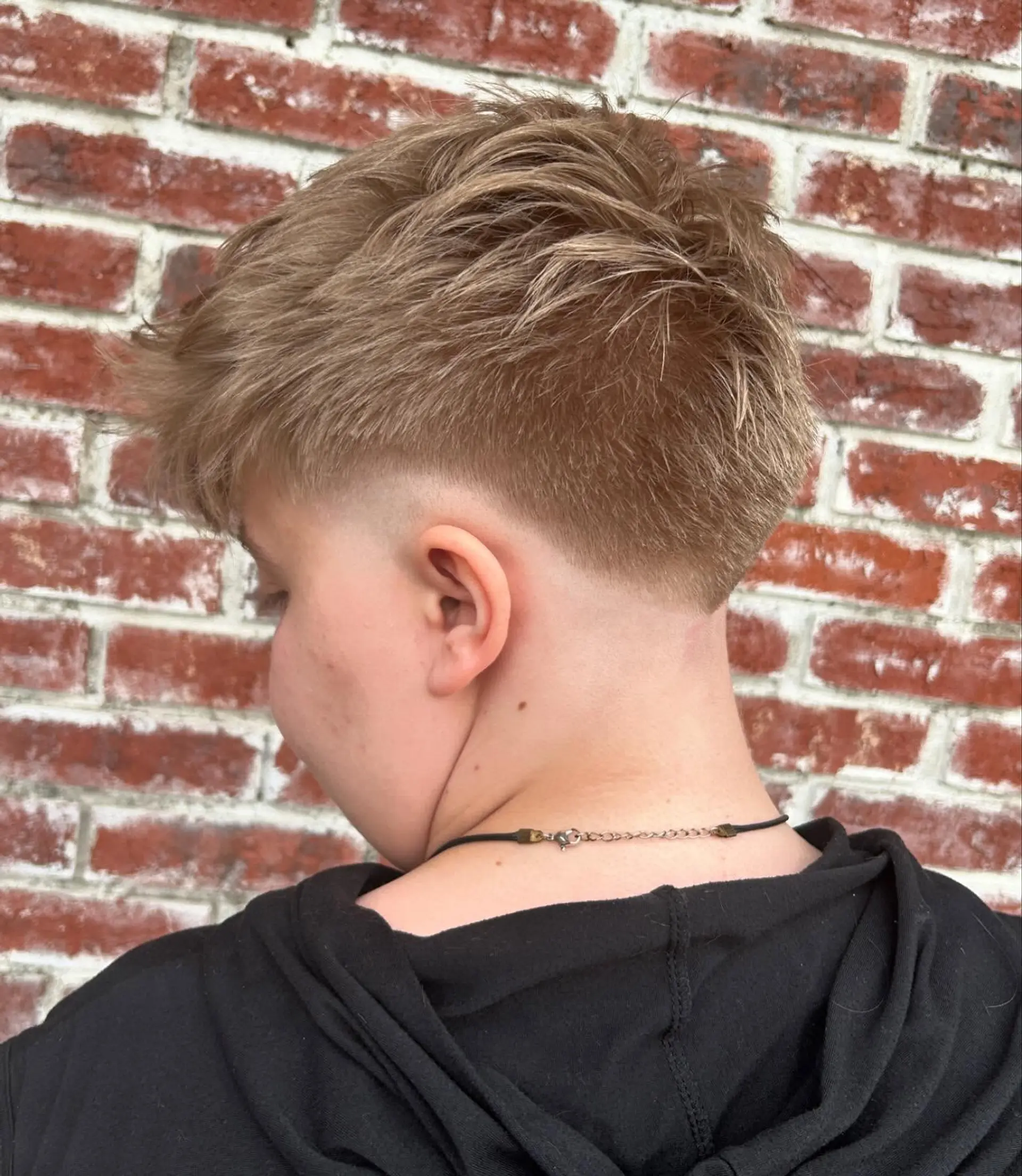 A short, modern textured crop styled with forward-swept texture on top and a clean low taper fade around the ear and neckline. 1