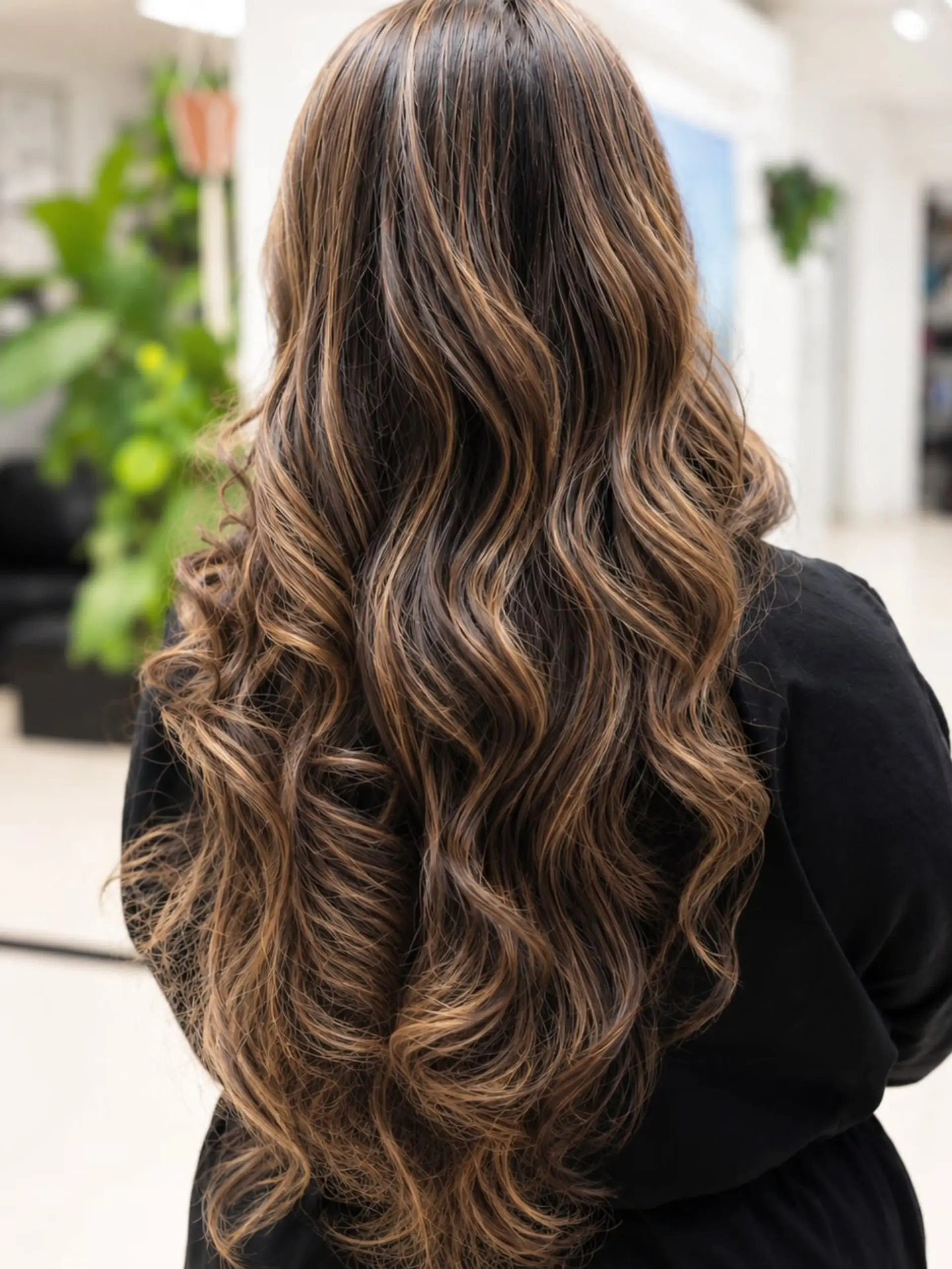 Long wavy dark brown hair featuring fine dimensional caramel and golden highlights throughout. 1