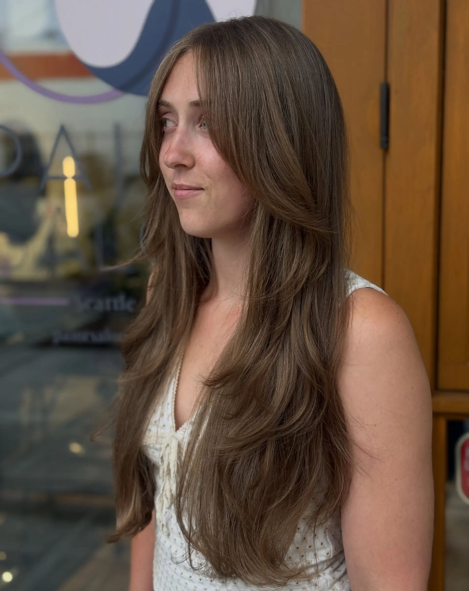 A long butterfly cut characterized by cascading, feathered tiers and soft face-framing layers starting around the jawline, styled with subtle turned-under ends for natural movement and volume. 1