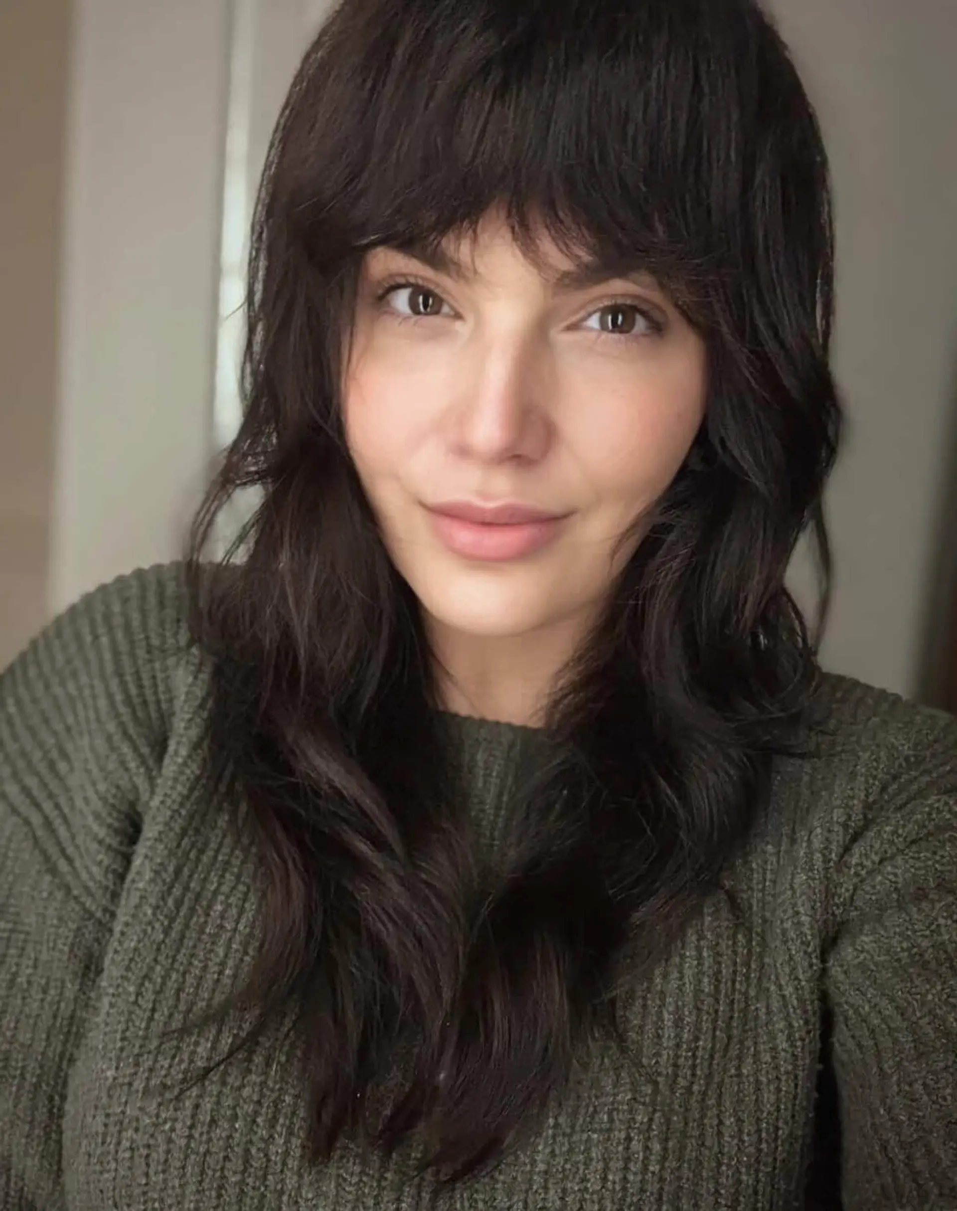 A long, textured brunette shag haircut featuring eyebrow-length full bangs and soft face-framing layers. 1