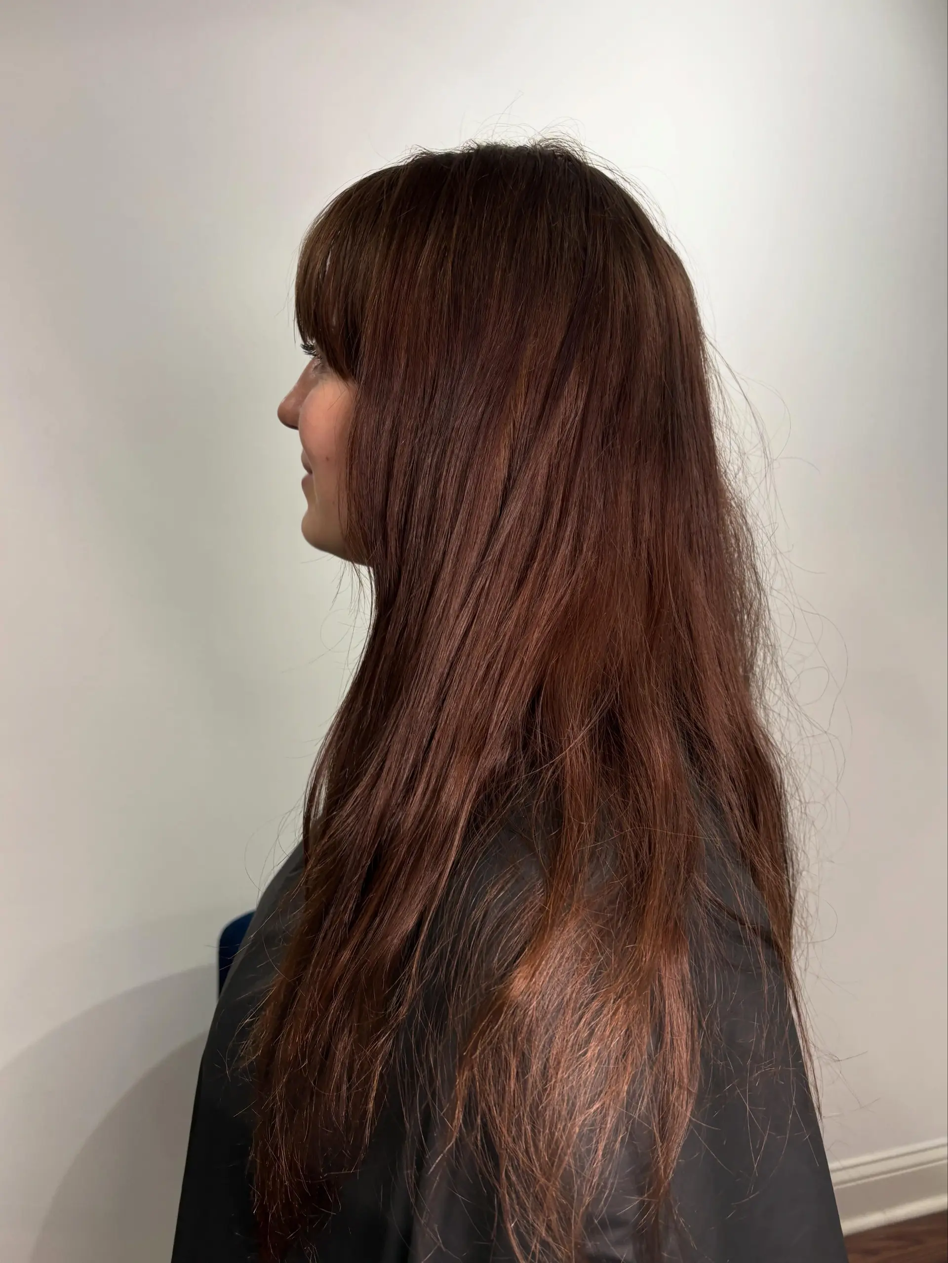 Long warm auburn-brown hair cut with full brow-grazing fringe bangs and subtle face-framing layers. 1