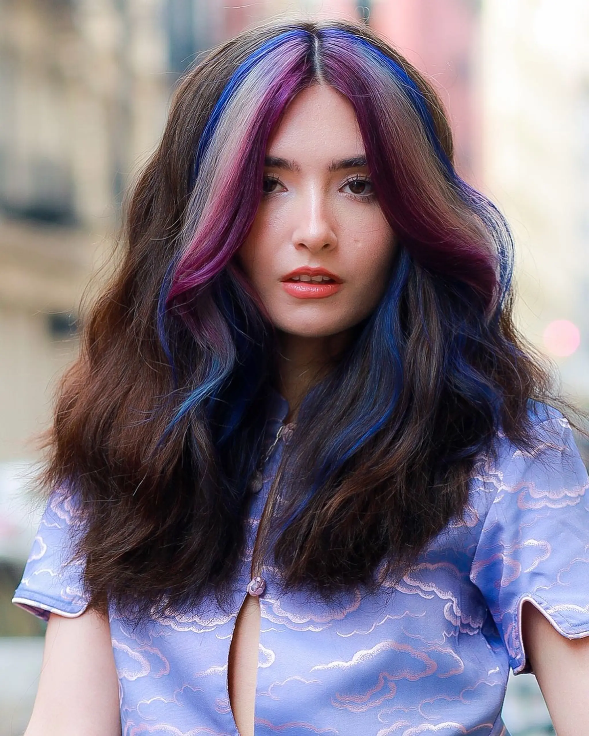 Long, wavy brown hair with voluminous waves and vibrant purple and blue highlights. The hair is parted in the middle, creating a striking and textured look.