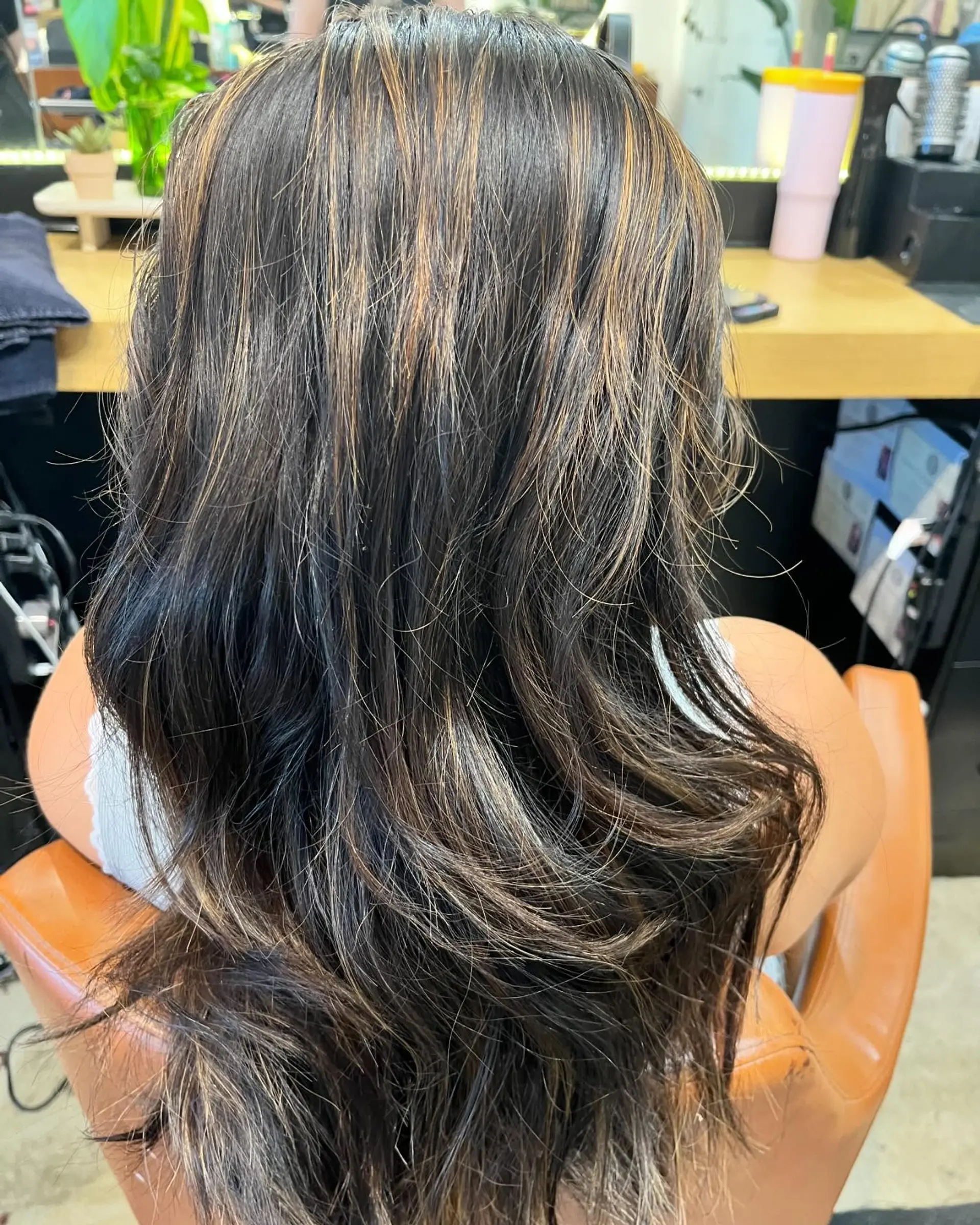 Long dark brown hair featuring subtle caramel and warm blonde highlights, styled in soft, layered waves. 1