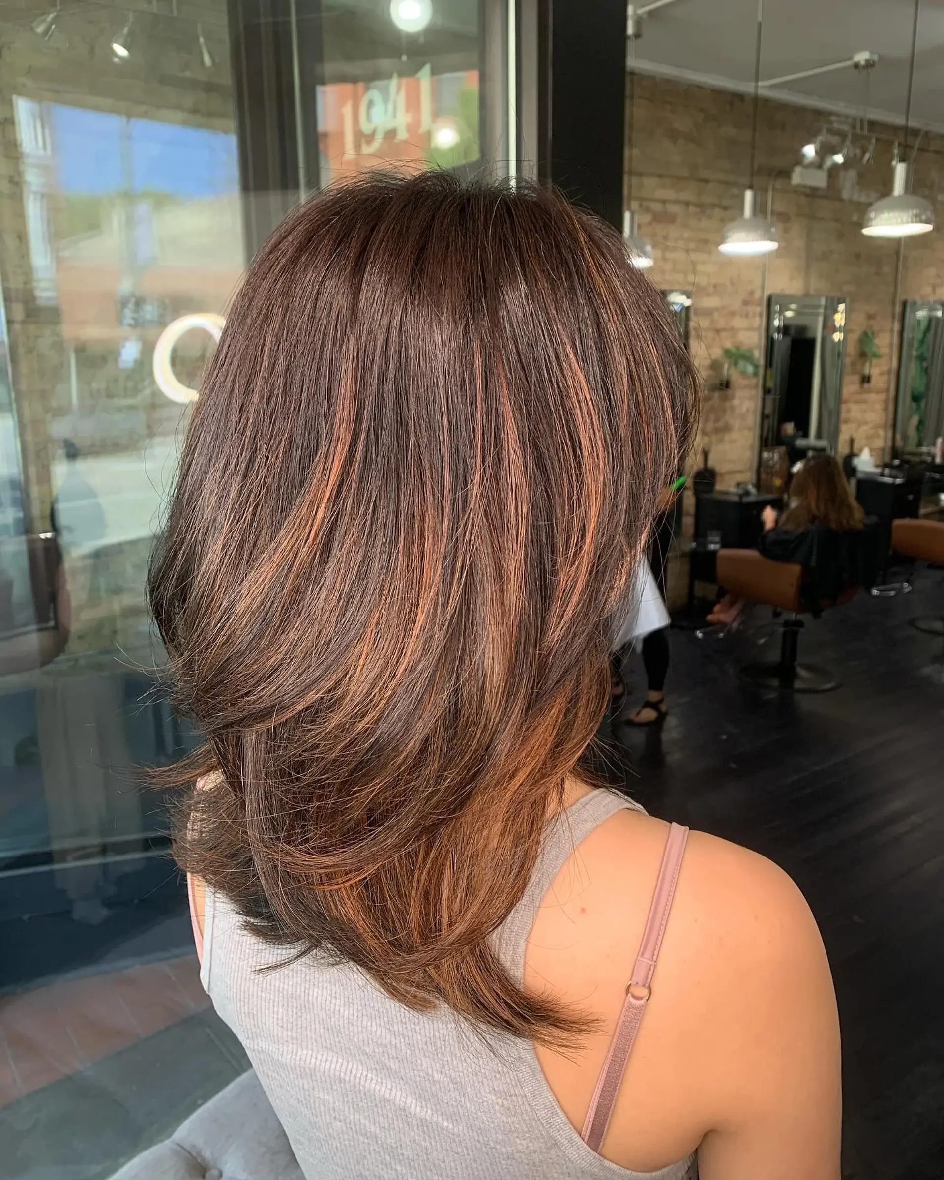 Medium-length layered brunette haircut accented with warm copper and caramel highlights, finished with a smooth blowout. 1