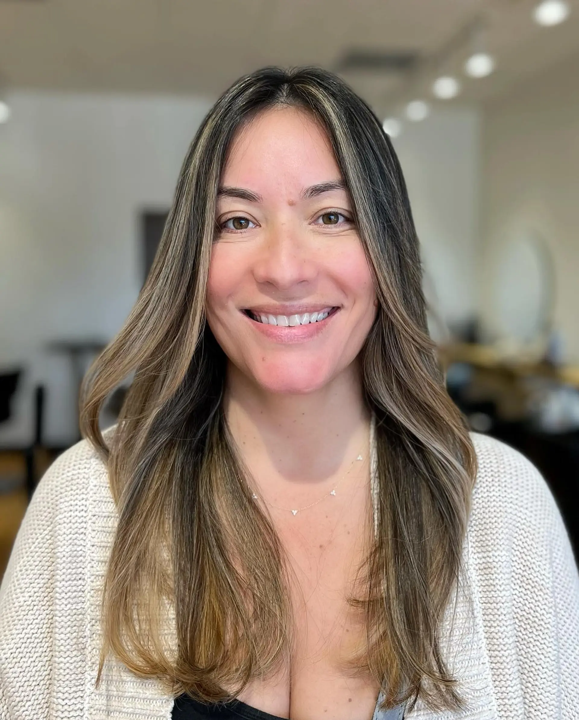 Long brunette hair featuring fine, sun-kissed blonde highlights blended seamlessly from root to tip with soft face-framing layers. 1