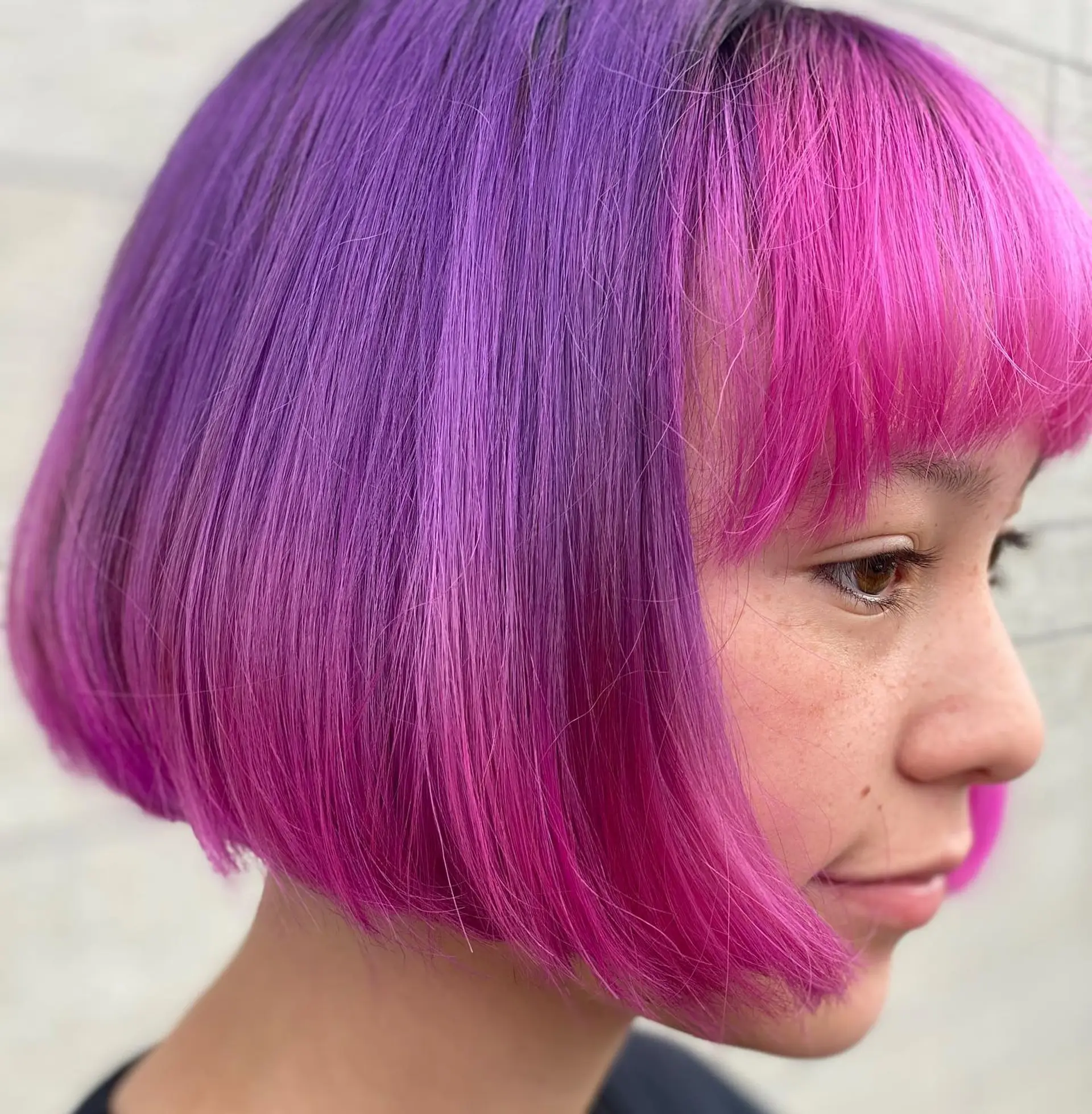 A blunt chin-length bob with straight bangs, showcasing a vivid color melt from purple roots to bright magenta pink ends. 1