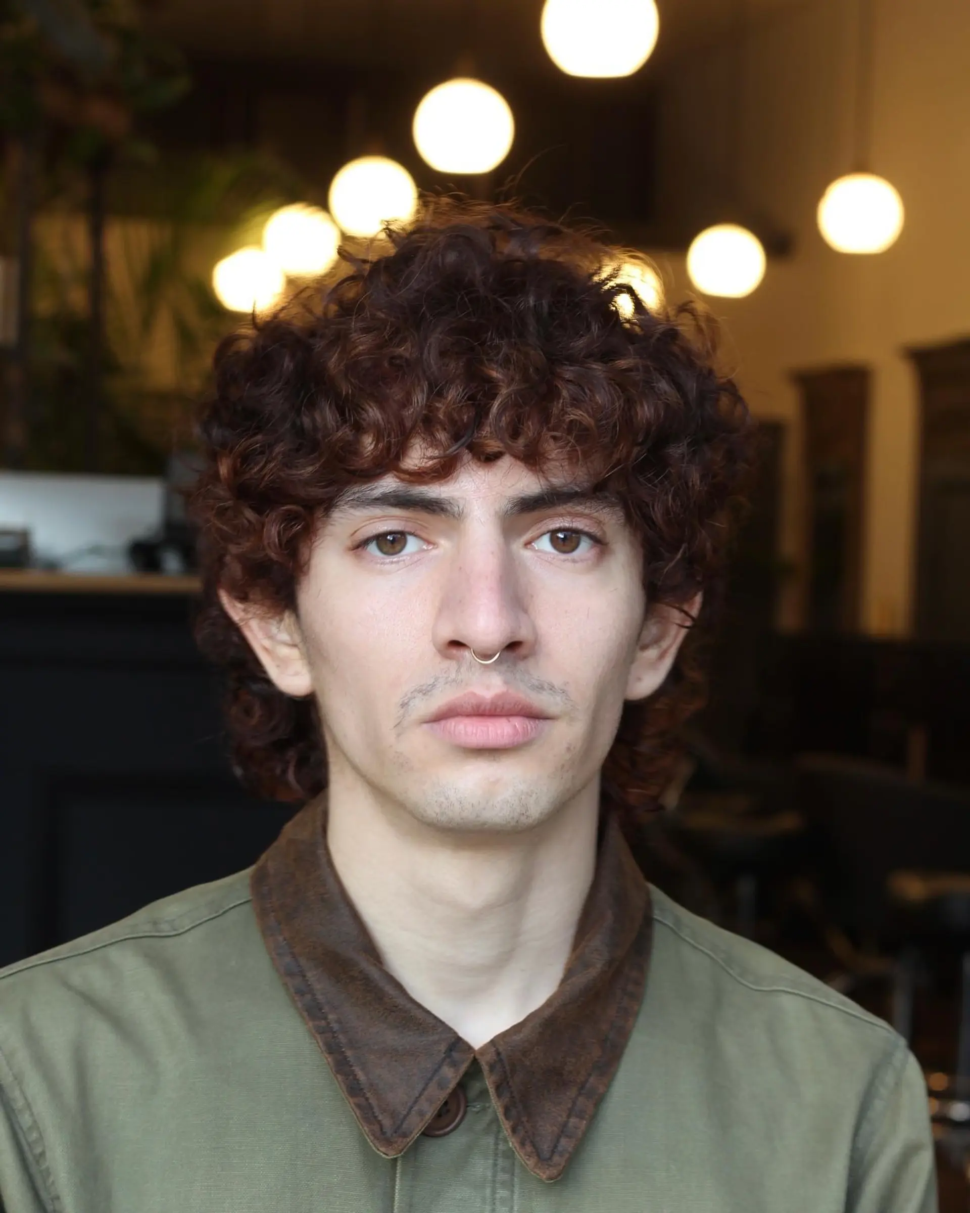A textured curly haircut with natural volume, rounded curly bangs, and soft length extending around the sides and nape. 1