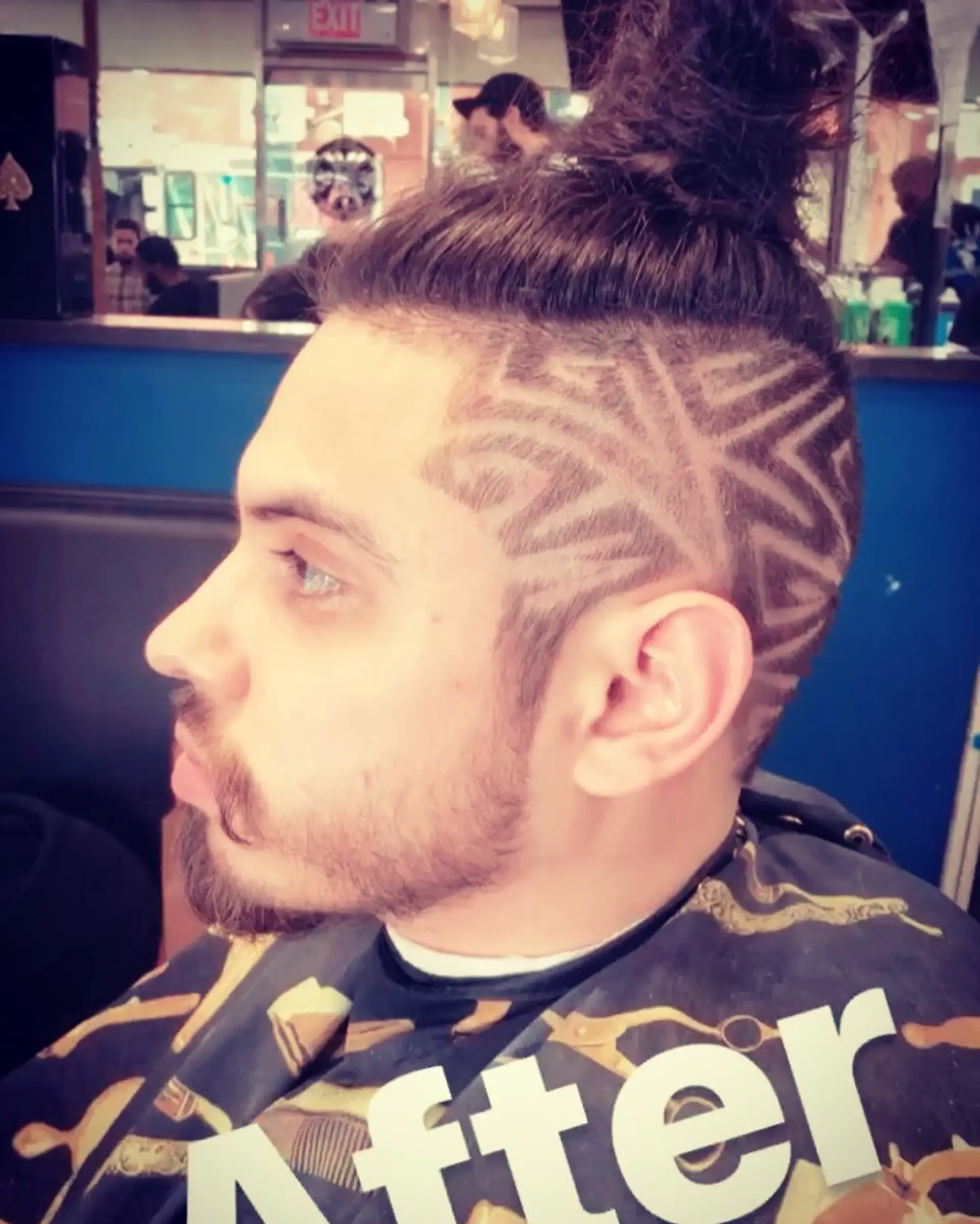 An undercut featuring an intricate geometric etched hair design along the shaved sides, paired with longer hair gathered into a high top knot. 1