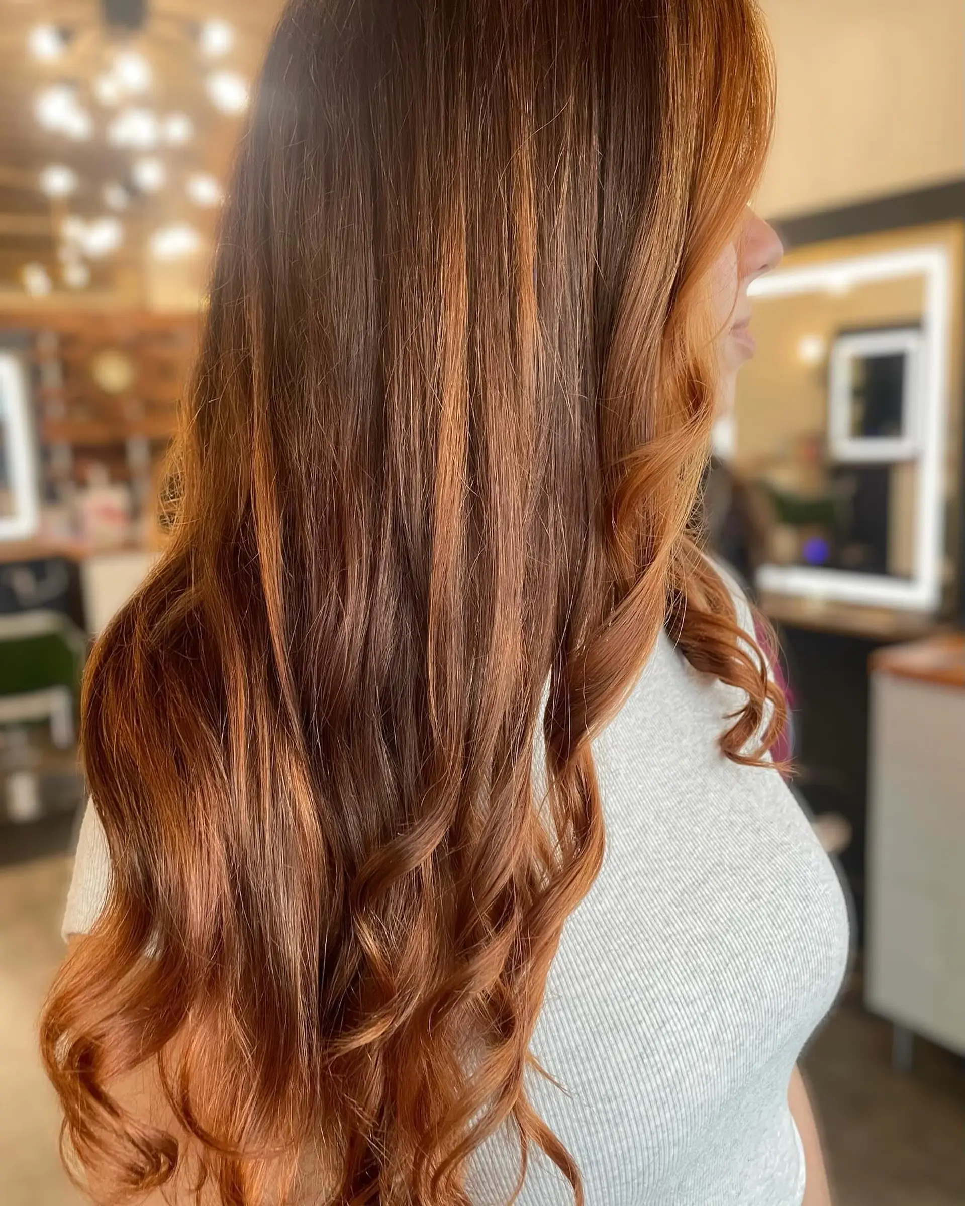 Long rich copper hair enhanced with dimensional balayage highlights and styled with soft curling iron waves at the ends. 1