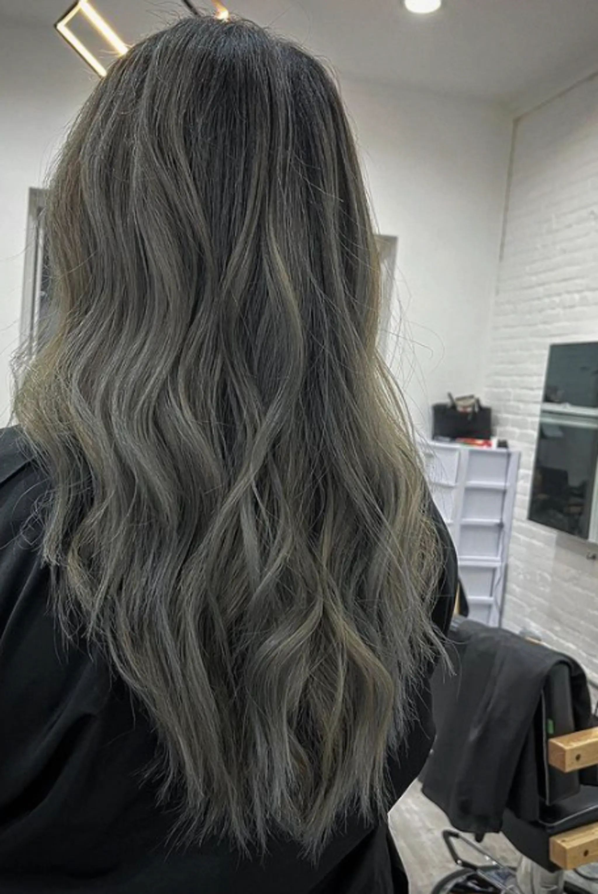 Long, wavy hair with a blend of gray, ash brown, and silver tones, featuring natural waves and subtle root shading for depth.