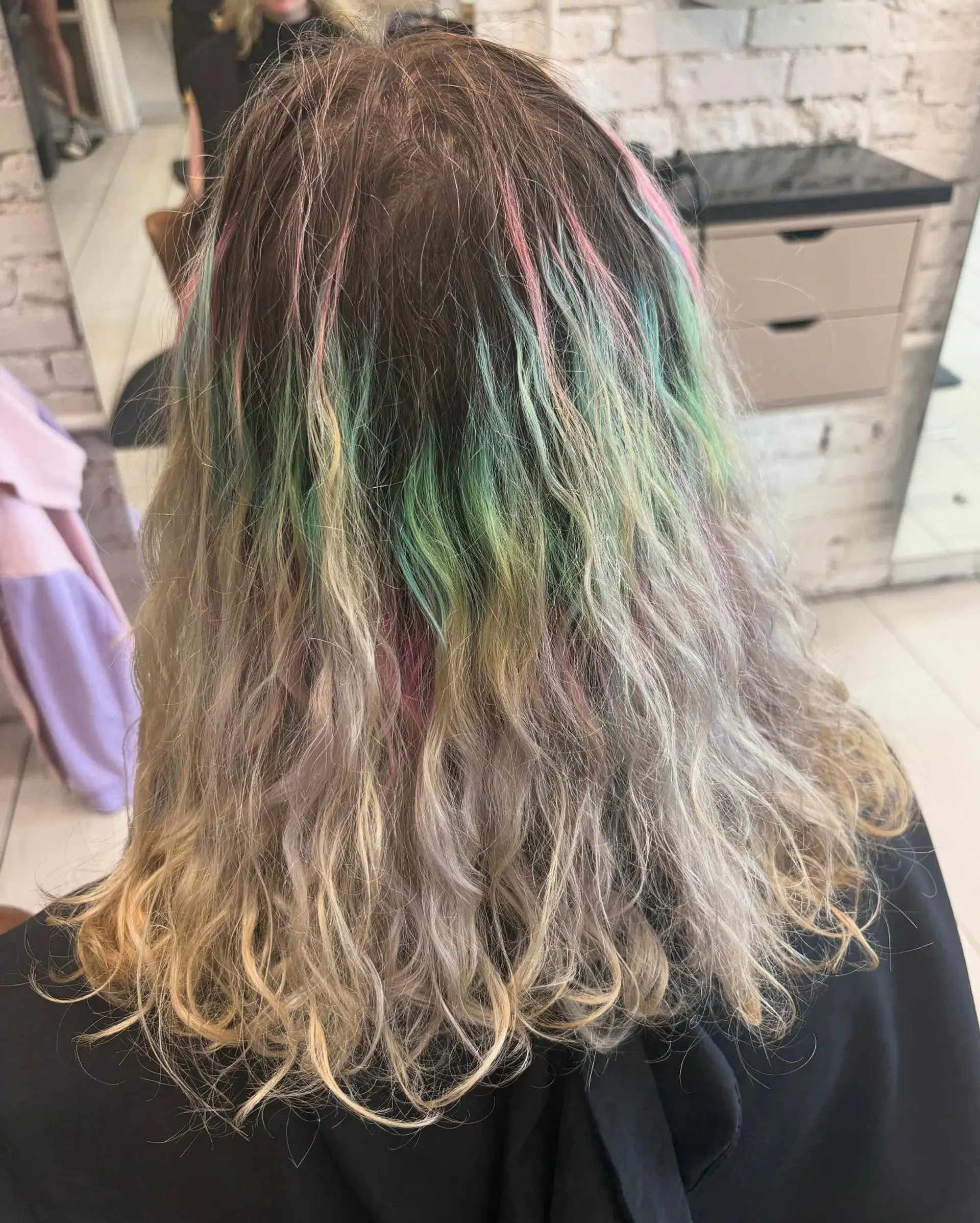 Medium wavy hair featuring multi-toned pastel streaks of pink and green blended through a dimensional blonde base. 1