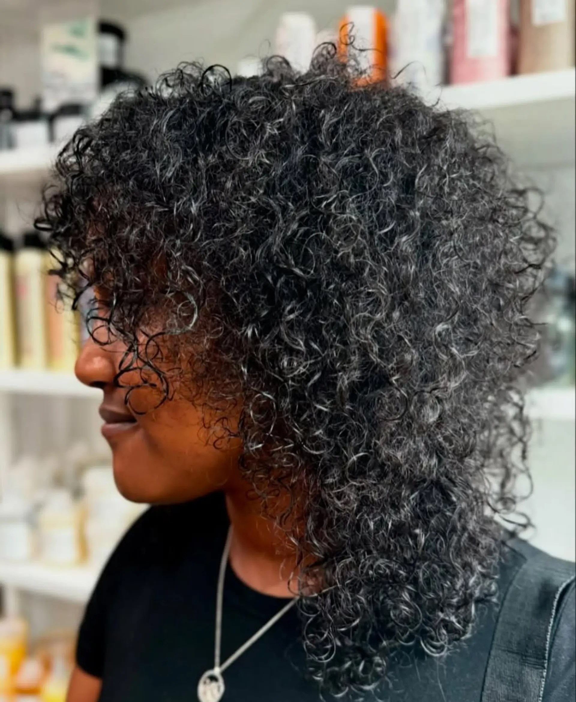 A voluminous, medium-length curly cut with dynamic layers and soft curly bangs that frame the face, celebrating natural texture and movement. 1