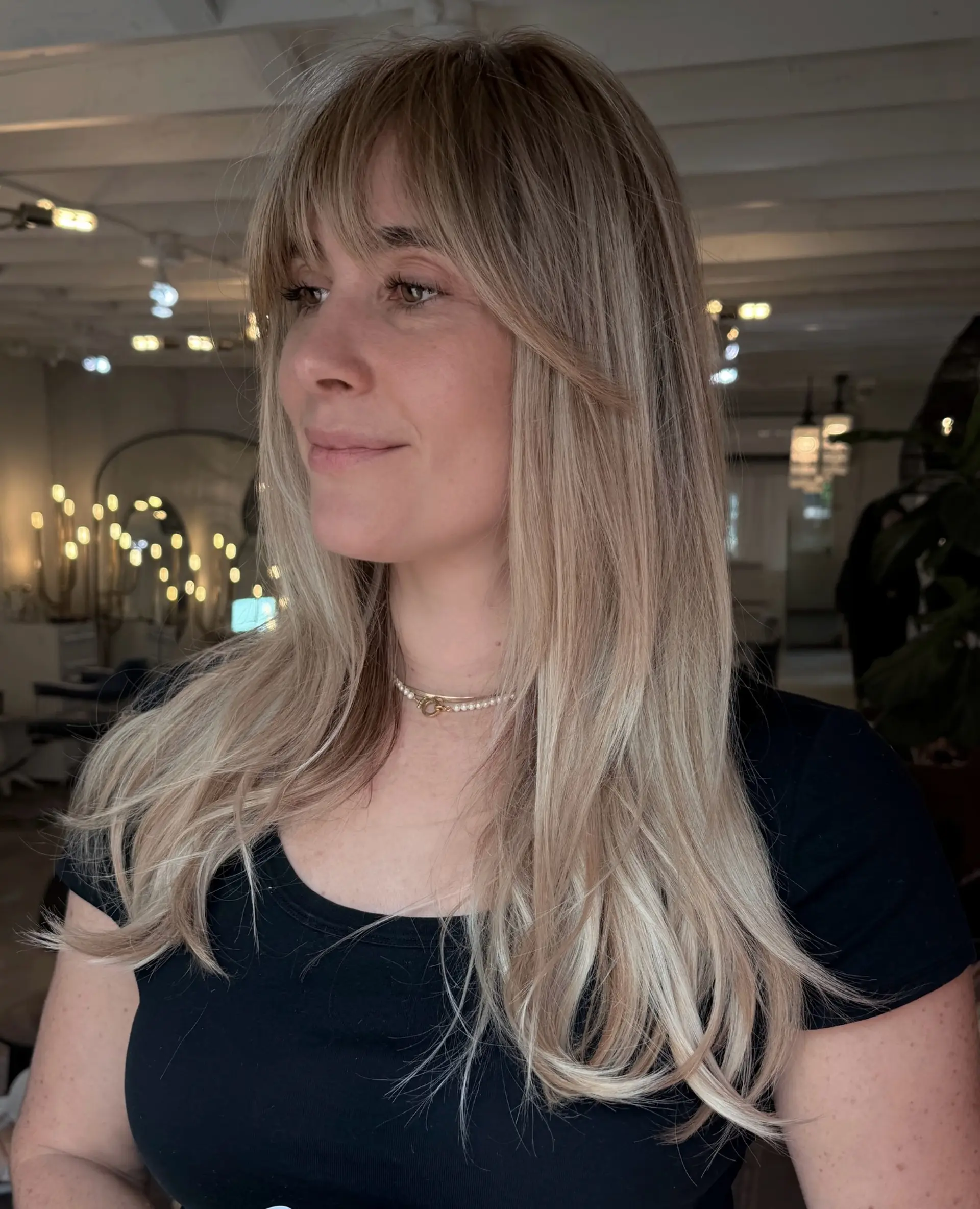Long beige-blonde hair with light layering and straight-across wispy bangs. 1