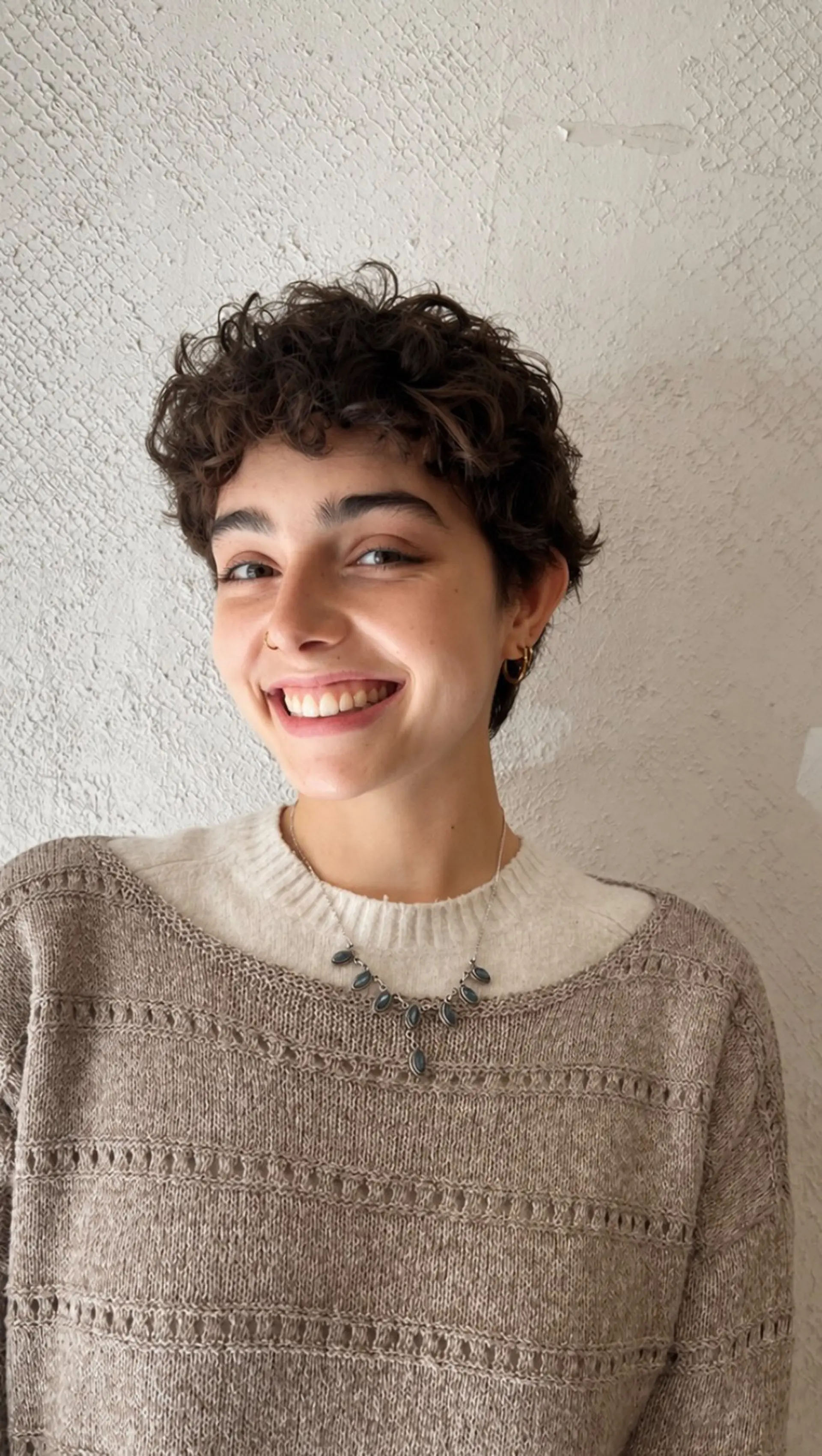 A short, textured curly pixie crop with defined curls framed softly across the forehead. 1