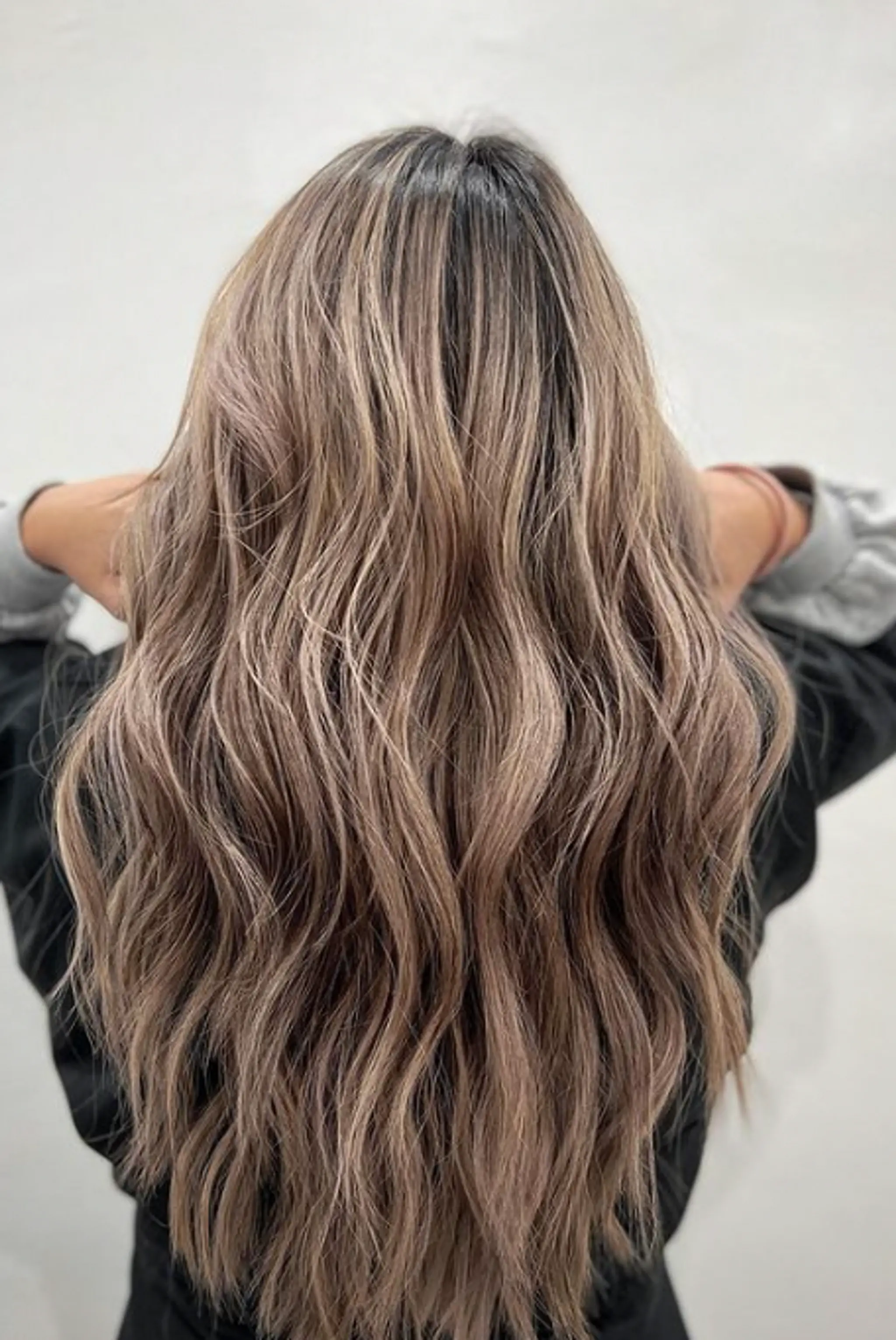 Long, naturally wavy hair with balayage combining blonde, ash blonde, and light brown tones. Loose, flowy waves create a soft, effortless look.